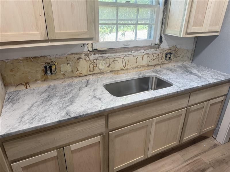 Kitchen countertop with marble pattern, sink, cabinets, and unfinished backsplash area