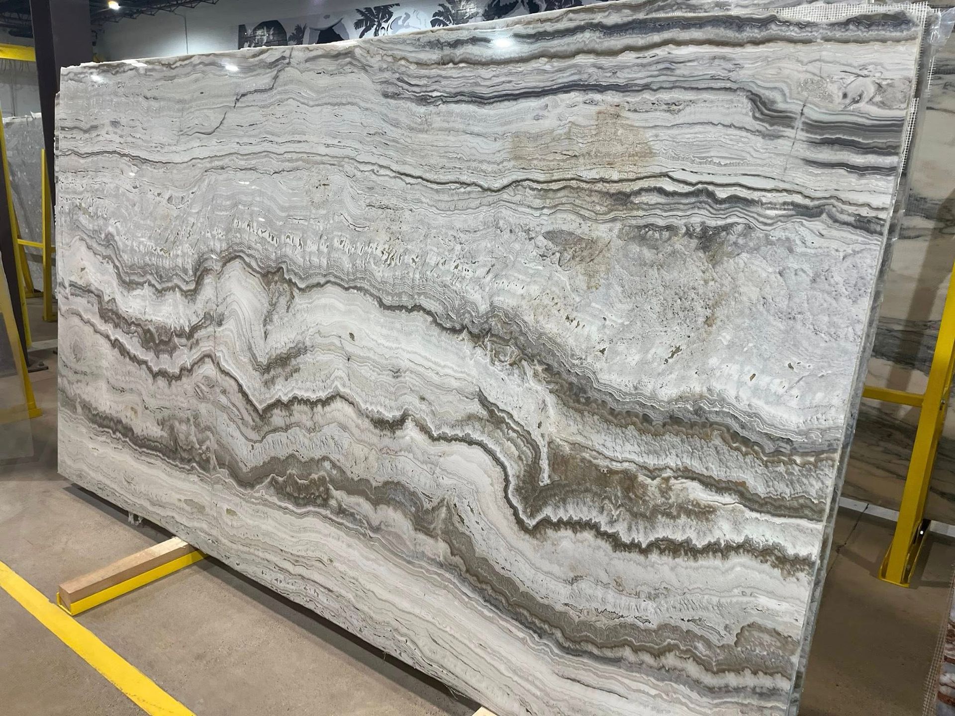 Large polished gray-and-white striped stone slab displayed upright in a warehouse-like setting