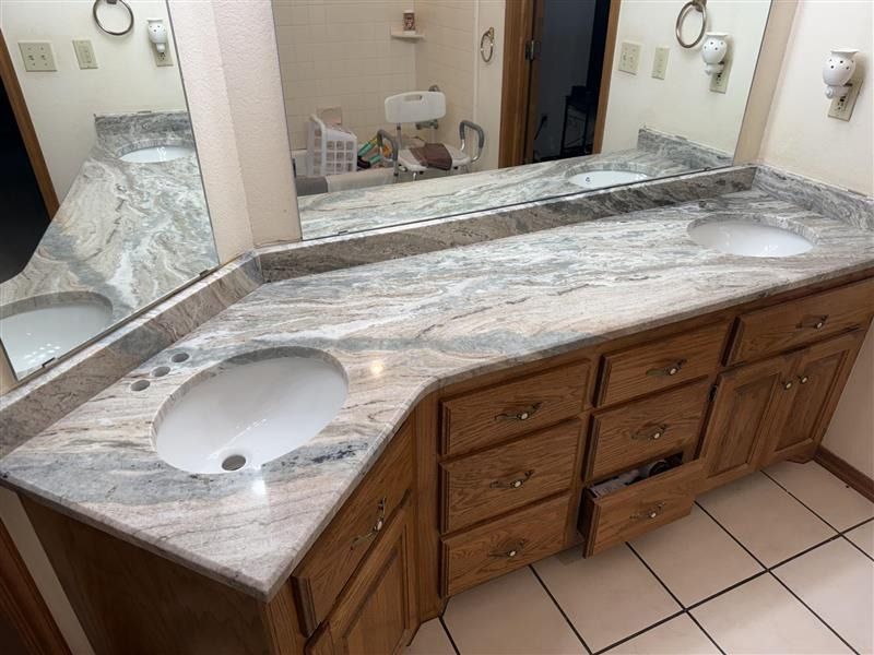Bathroom vanity with double sinks, marble countertop, wood cabinets, and large mirror