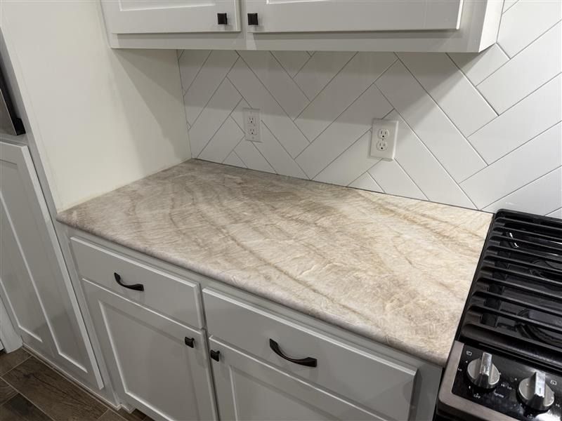 White kitchen counter with gray cabinets and herringbone tile backsplash near a stove