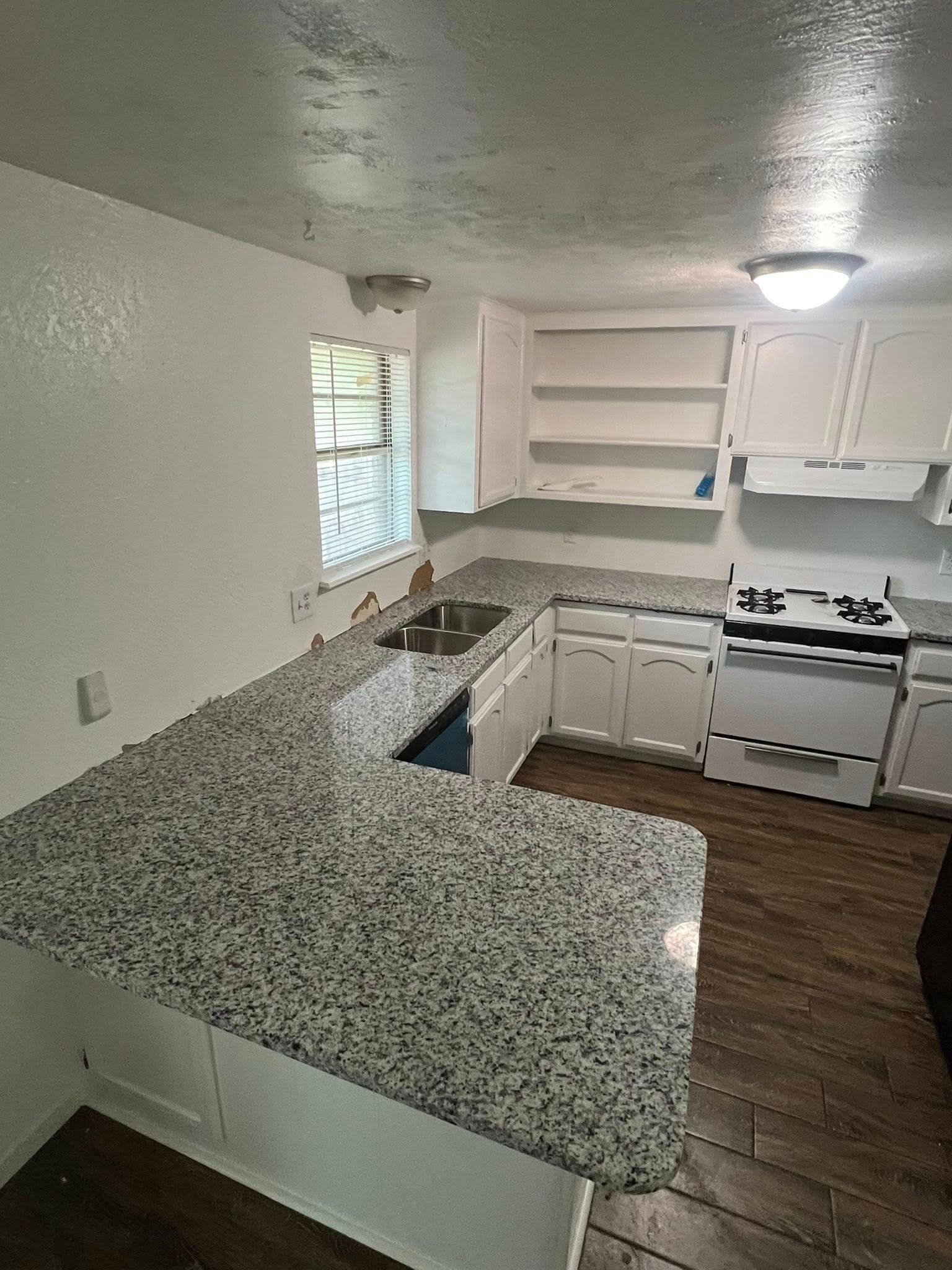 Small kitchen with white cabinets, speckled granite counters, gas stove, and wood-look floor.