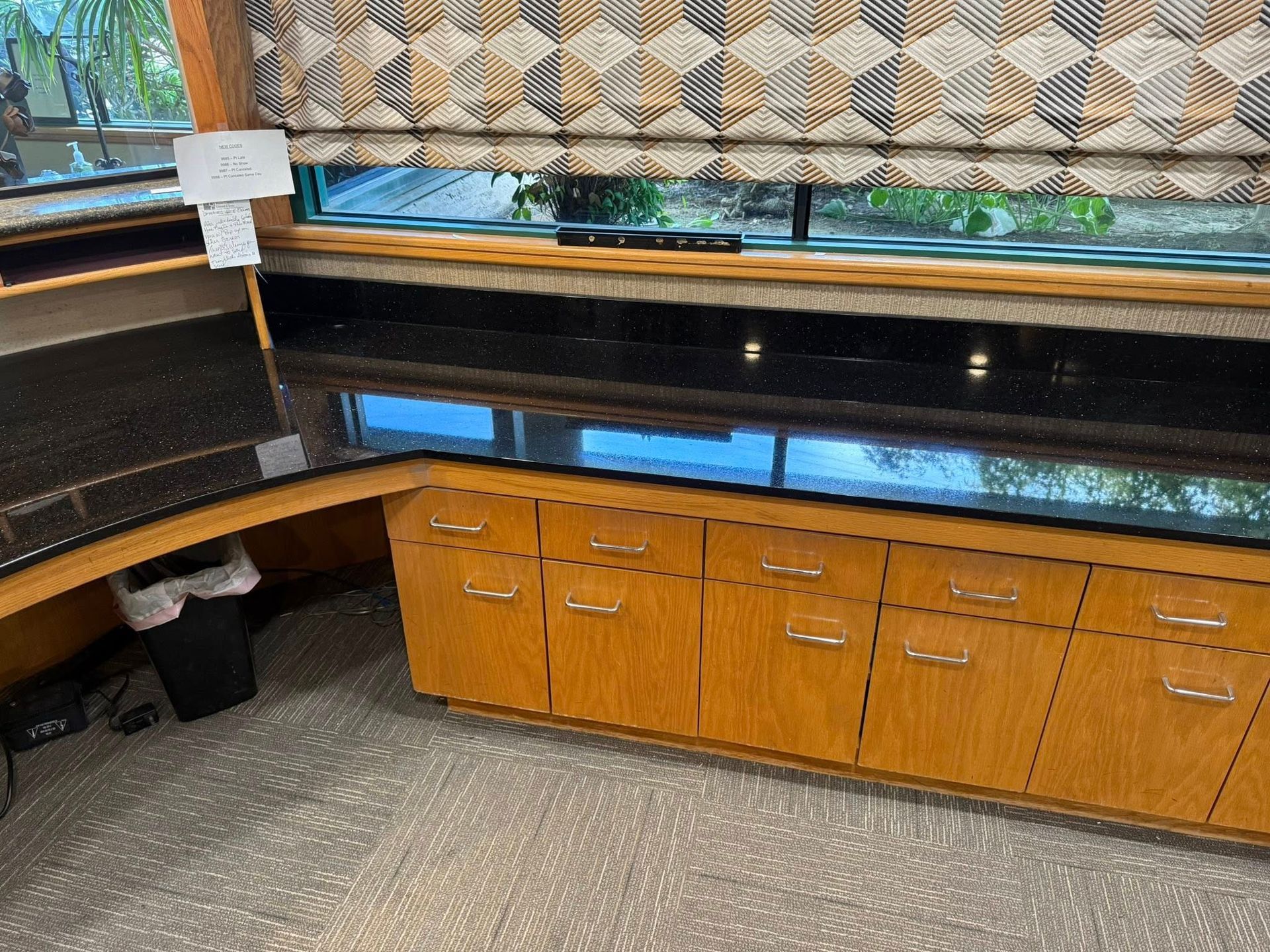 Kitchen counter with orange cabinets, black countertop, and patterned window blinds.