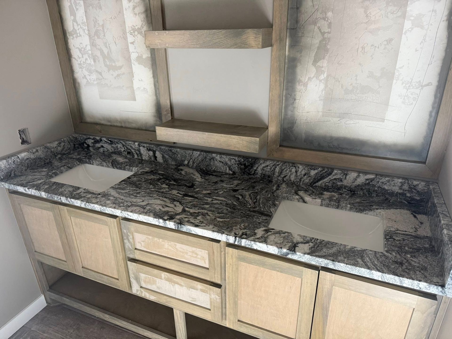 Unfinished kitchen vanity with dark granite countertop, double sink cutouts, and beige cabinets under a wall niche
