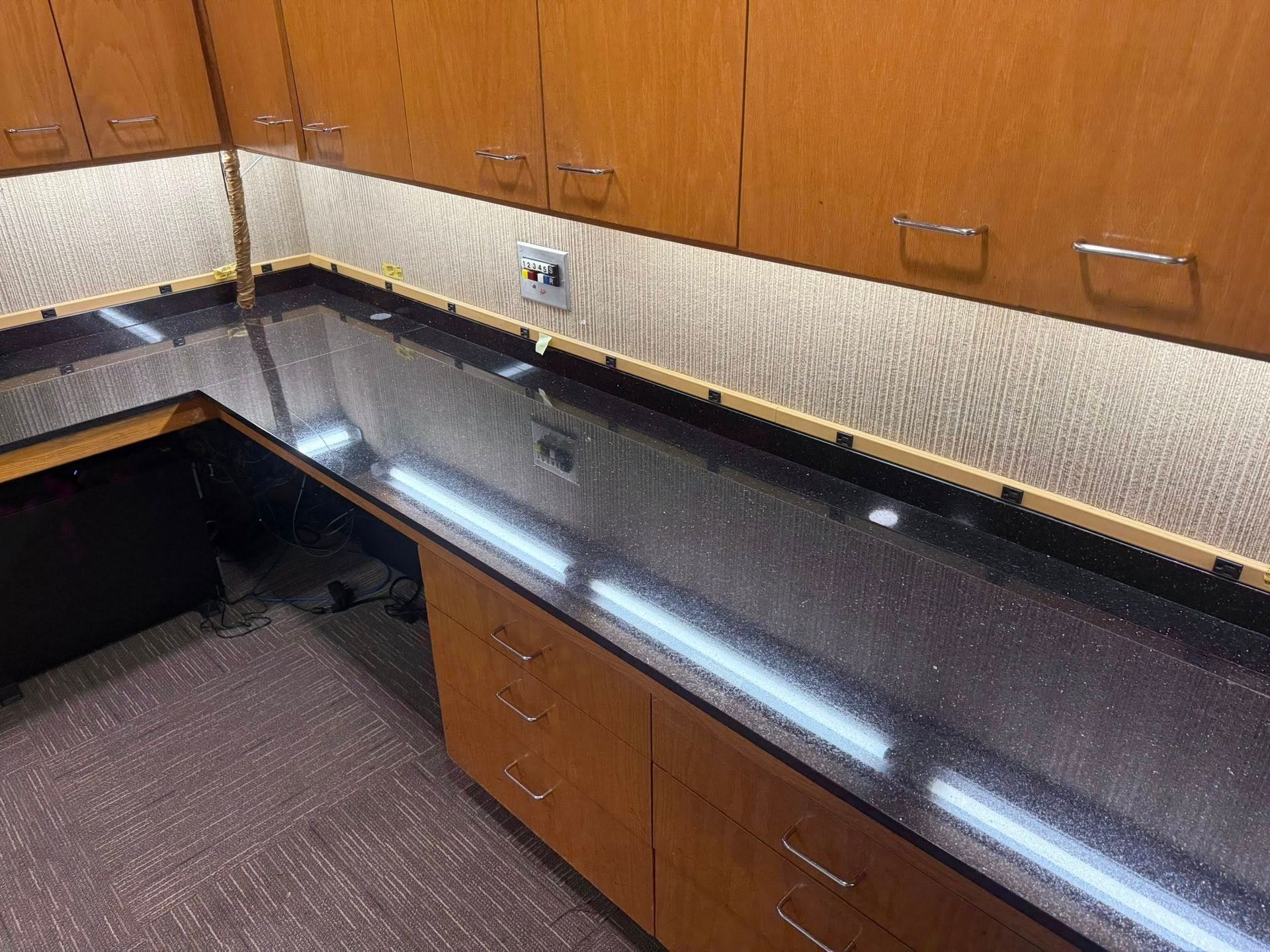 Office kitchenette with black countertops, wood cabinets, and a peninsula workspace