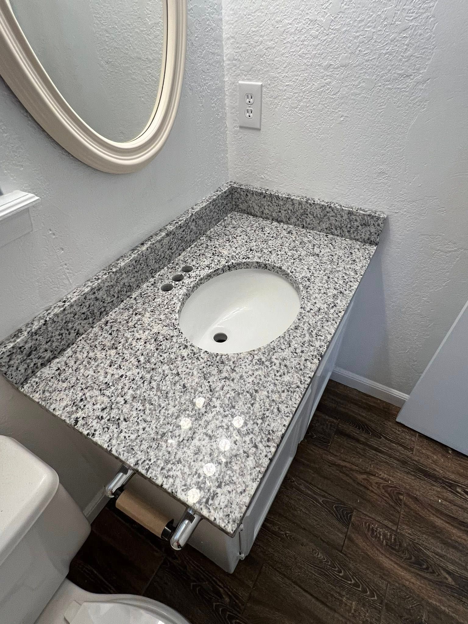 Bathroom vanity with speckled granite countertop, oval sink, and wall-mounted mirror