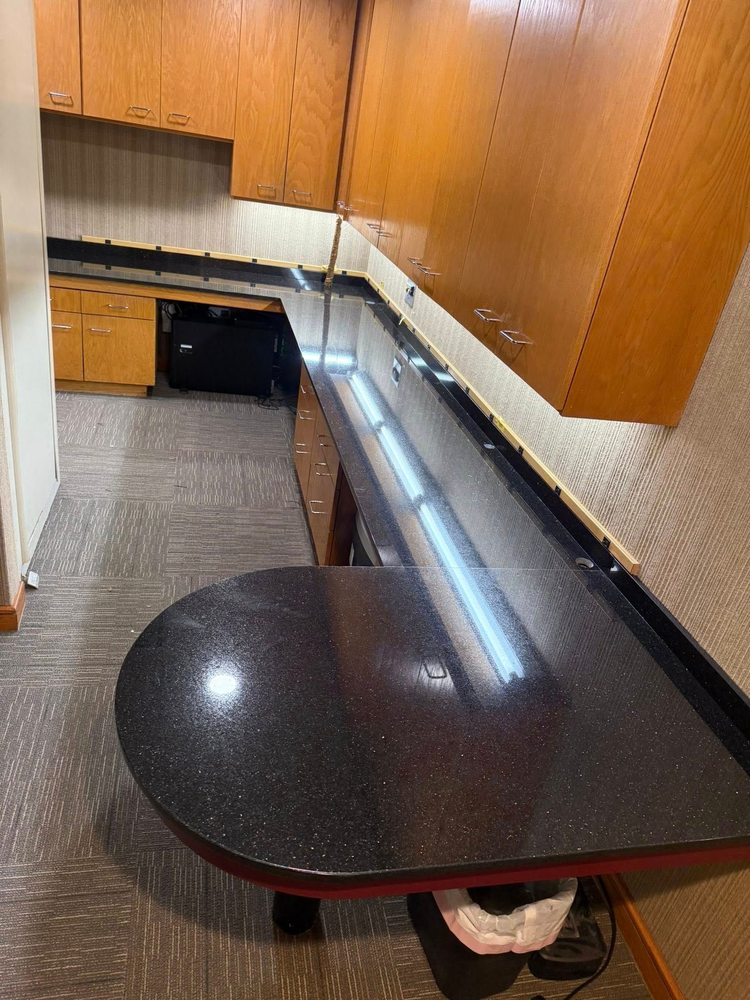 Small kitchen nook with wood cabinets, black countertop, and carpeted floor.