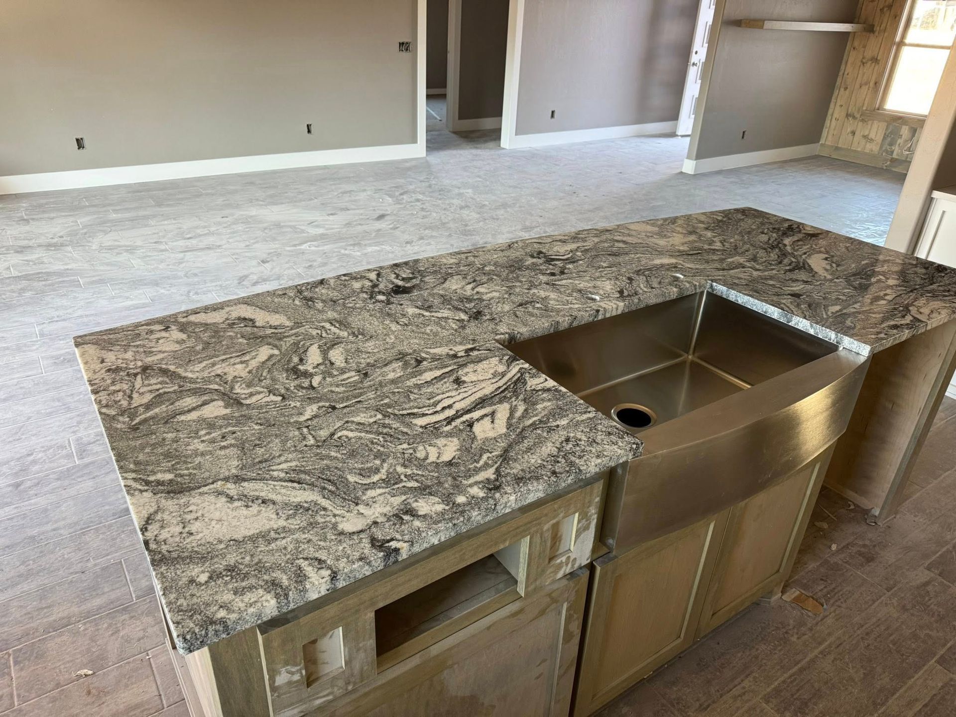 Kitchen island with granite countertop and stainless steel sink in an unfinished room