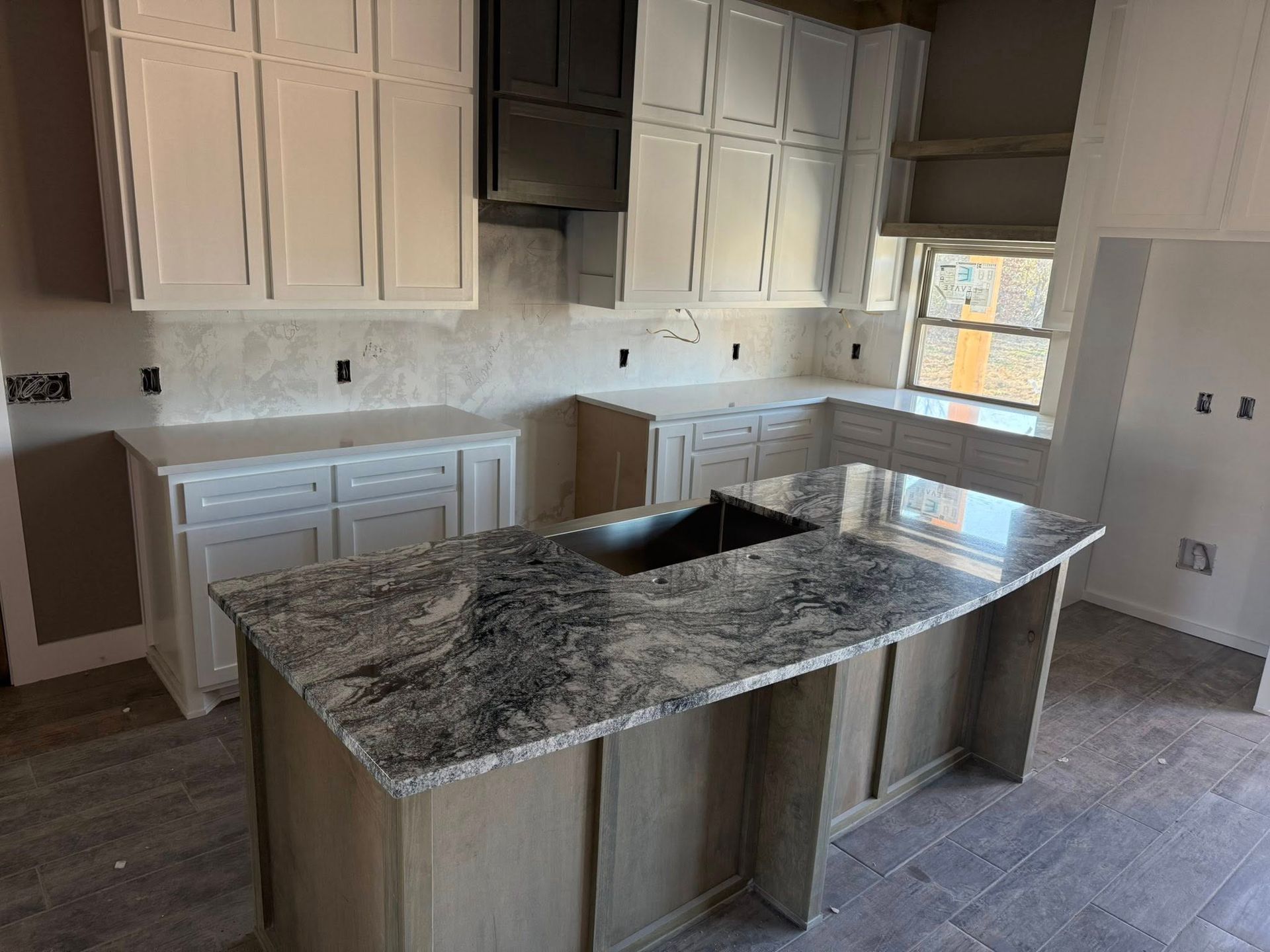Modern kitchen with white cabinets, granite island, and tiled floor under construction.