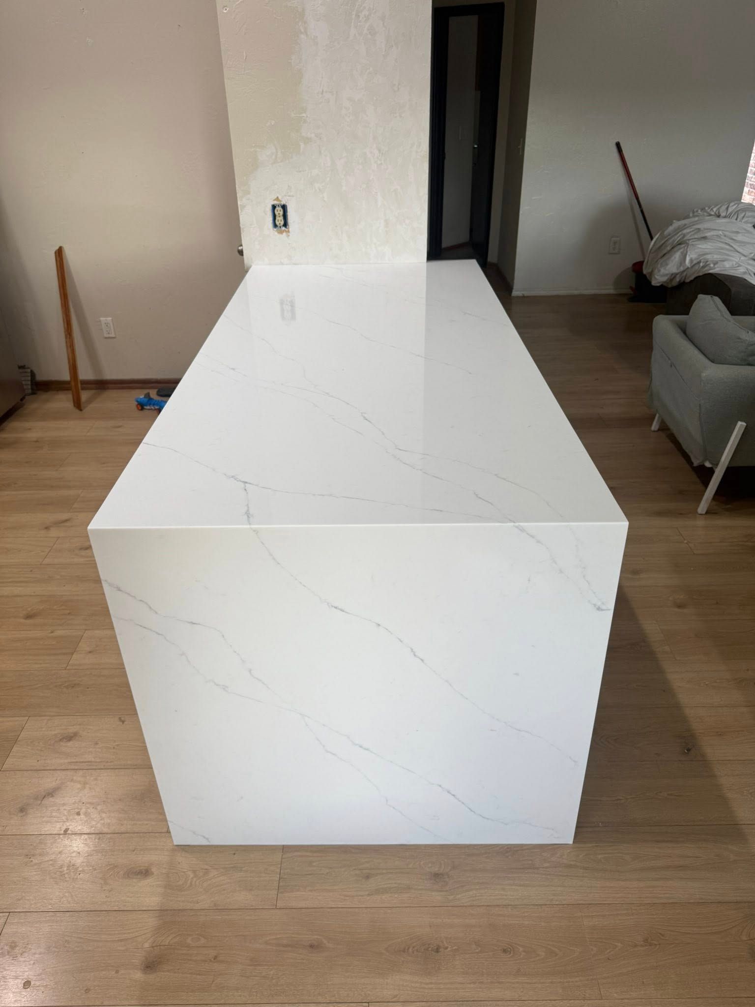 White marble-look countertop or island in a living room with wood floor and a gray sofa in the background