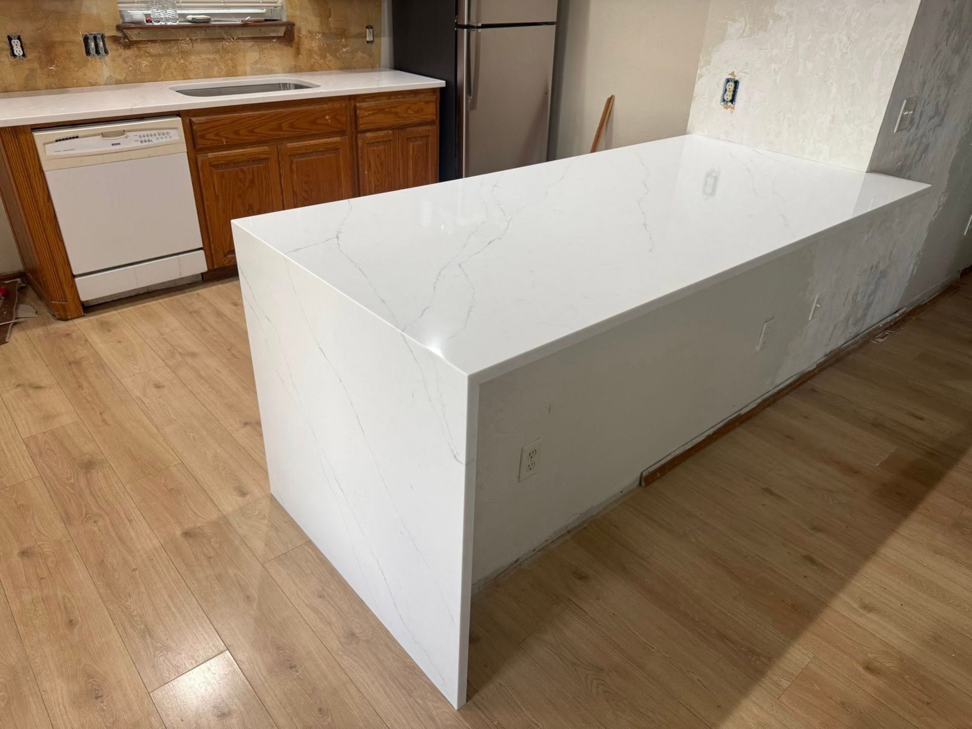 White kitchen island in an unfinished kitchen with wood cabinets and light wood flooring