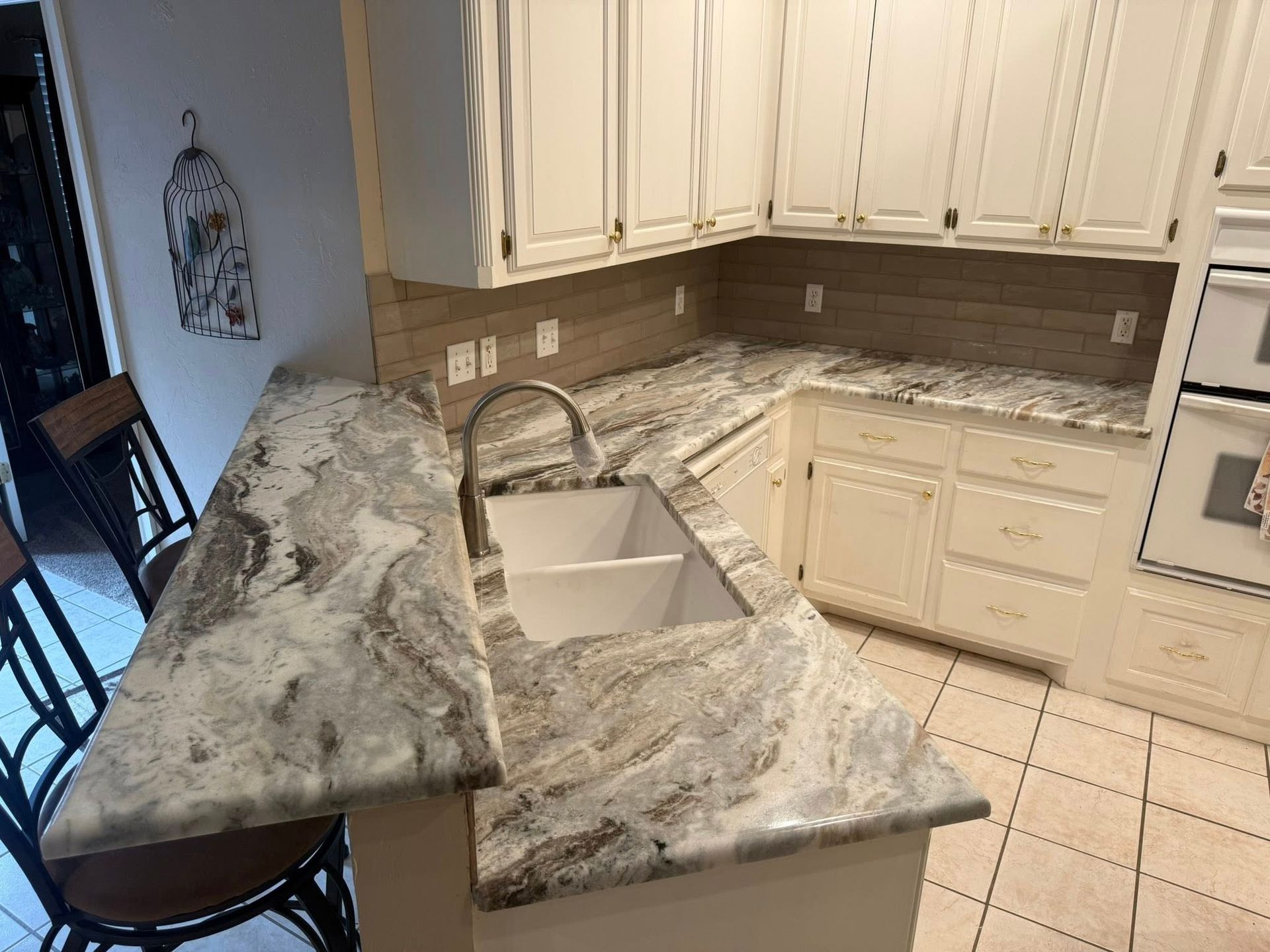 Kitchen with white cabinets, tiled floor, and a large marble-patterned peninsula counter.