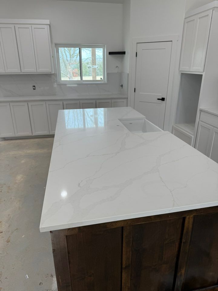 Bright modern kitchen with white marble island, white cabinets, window, and dark wood base cabinets