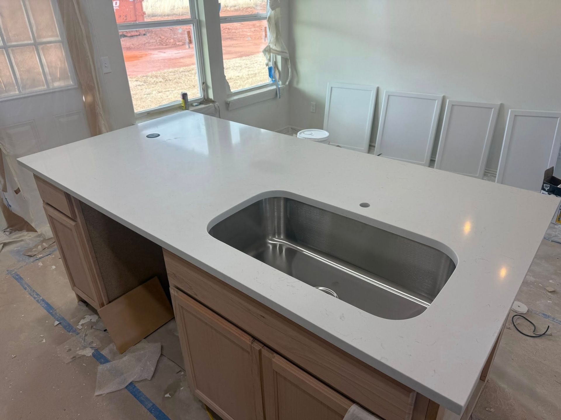 Kitchen island with white countertop and stainless-steel sink under construction near a window.
