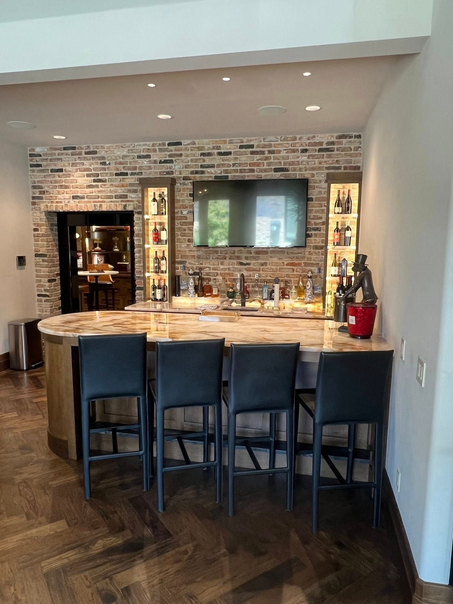 Home bar with four black stools, stone backsplash, and a mirrored wall in a modern kitchen.