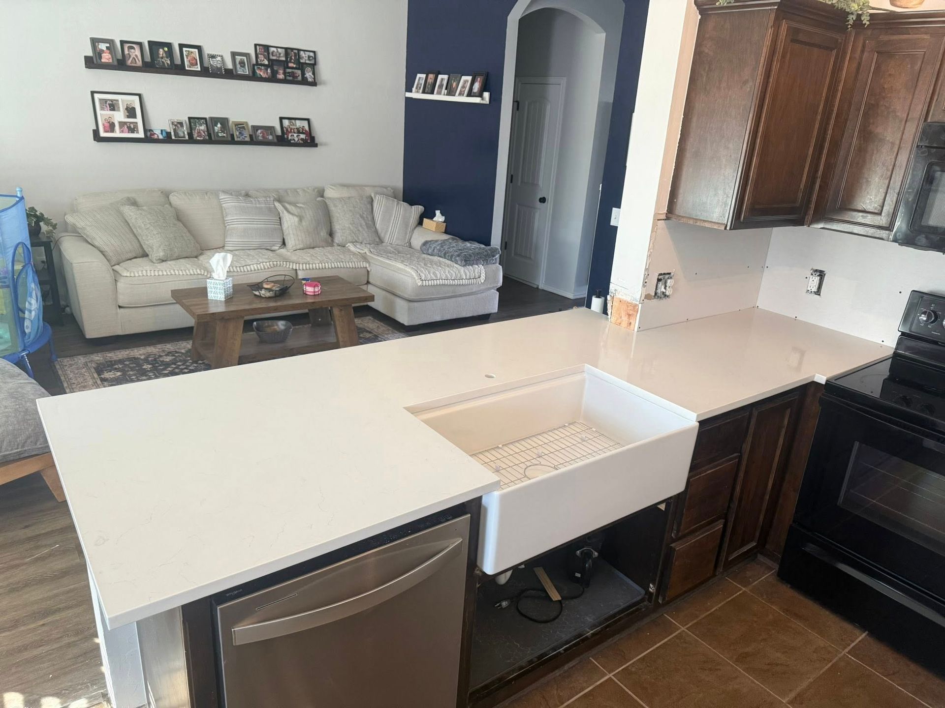 Modern kitchen with white island and sink, dark cabinets, and living room with gray sofa in the background