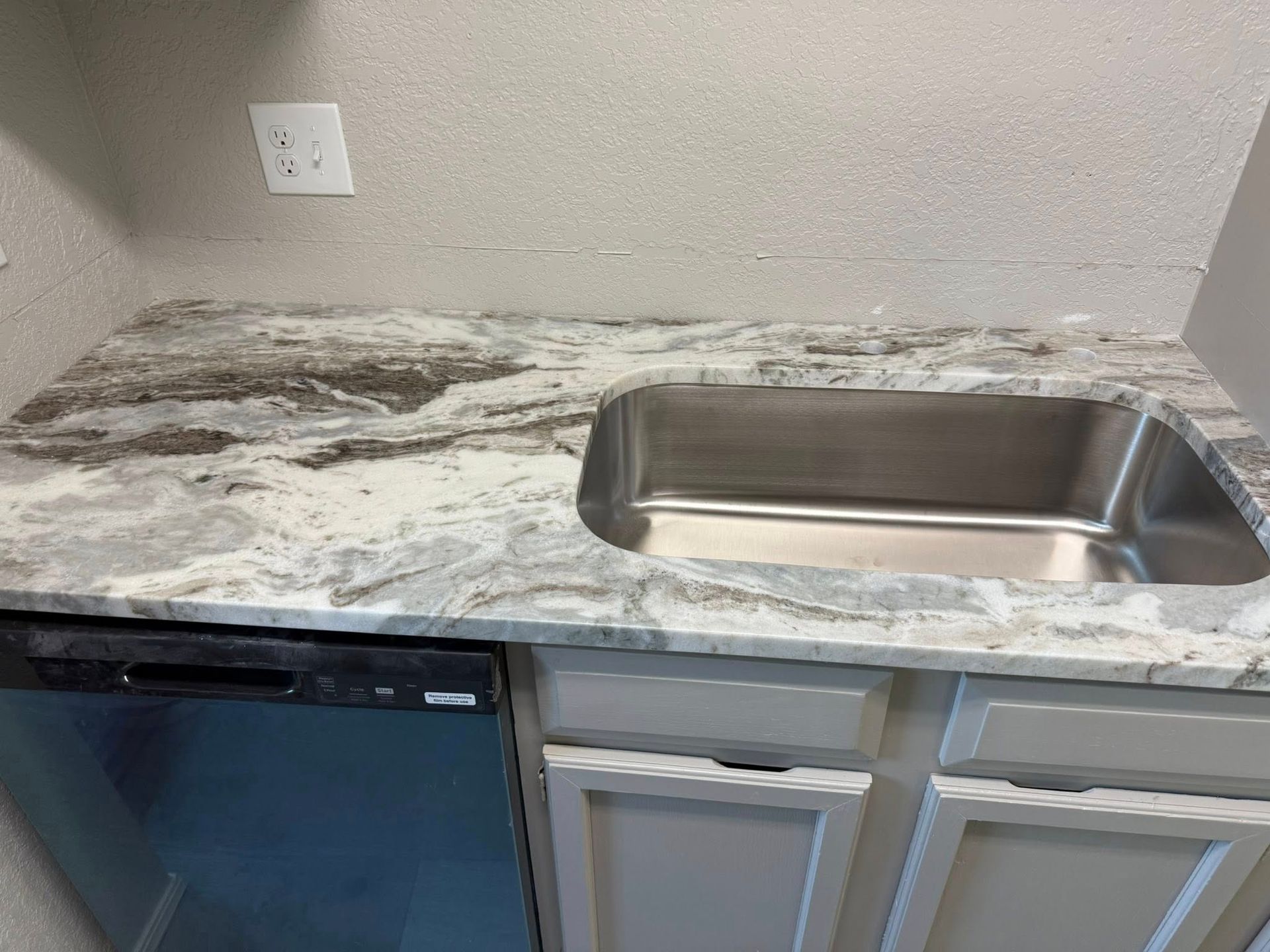 Small kitchen counter with speckled marble countertop, stainless sink, mini fridge, and gray cabinet doors.