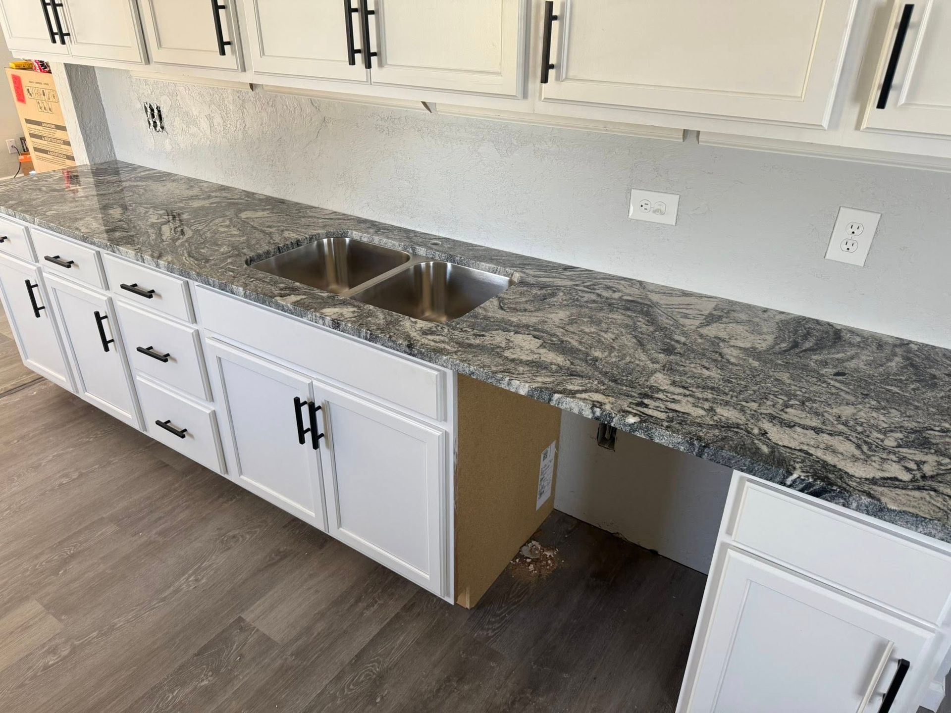 Kitchen with white cabinets, granite countertop, double sink, and an unfinished cabinet opening underneath.