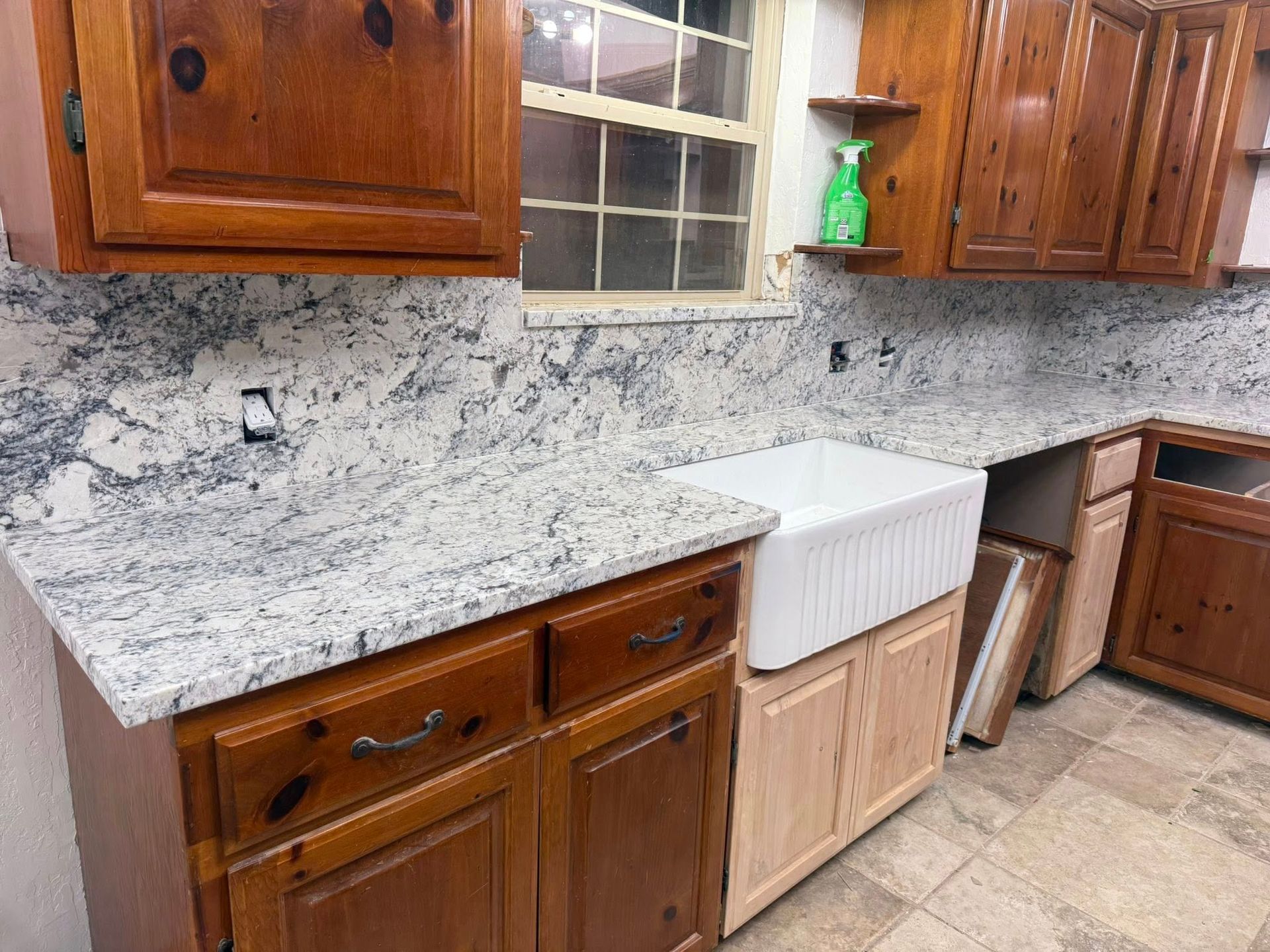 Kitchen with wood cabinets, marble-look countertop, and a white sink under a window.