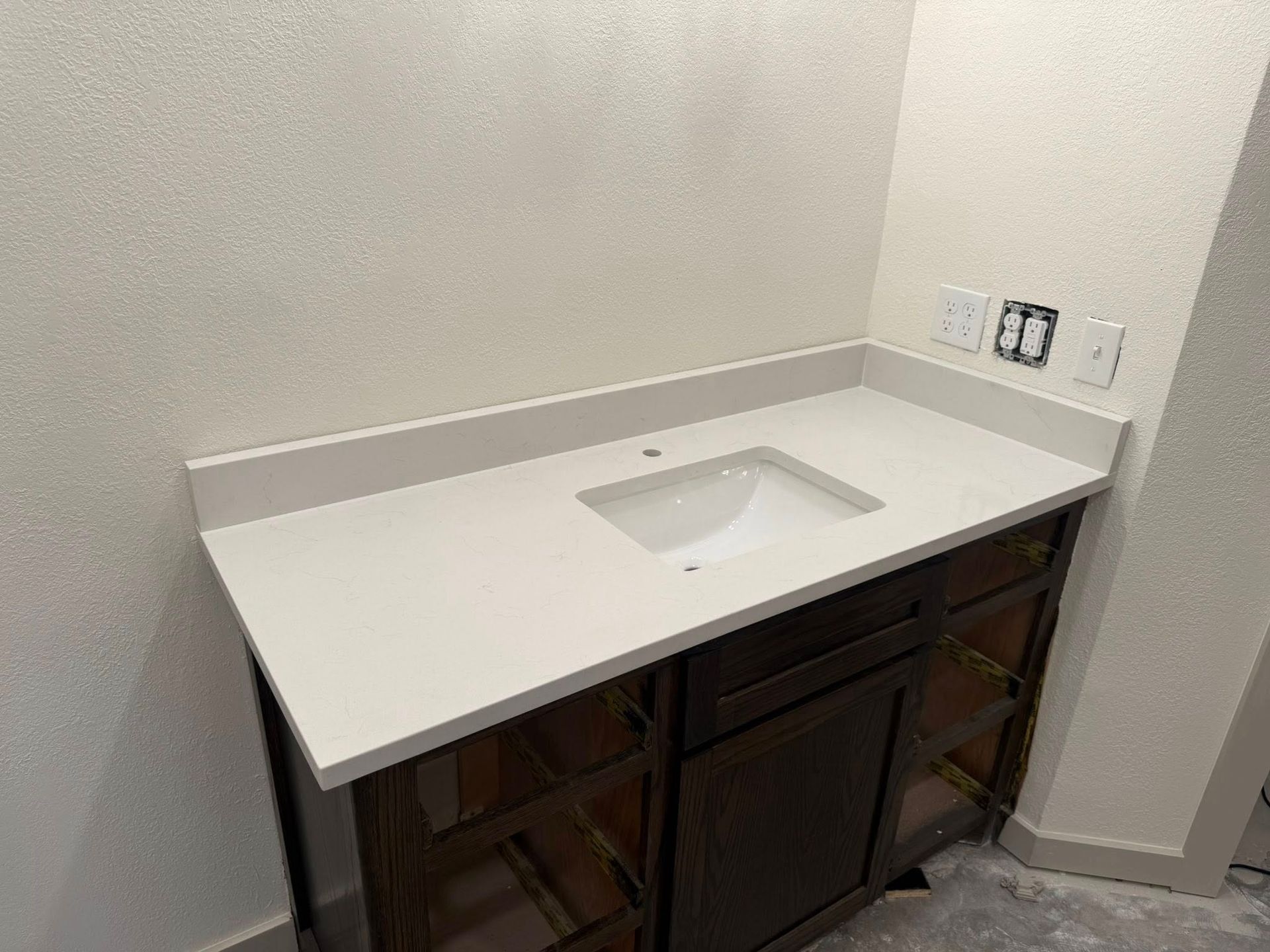 White bathroom vanity with integrated sink and dark wood cabinets against a light wall.