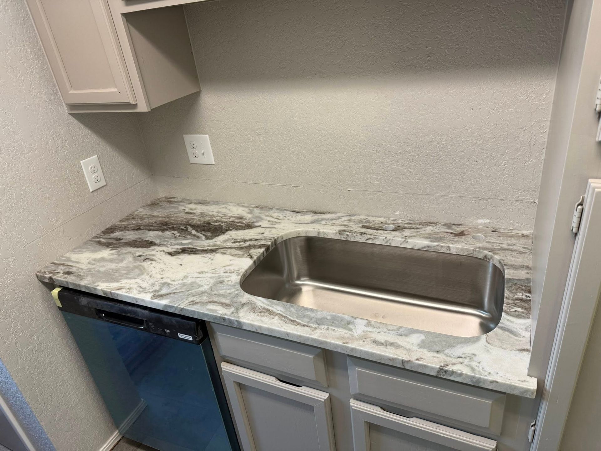 Compact kitchenette with granite countertop, stainless sink, and blue mini fridge in a small gray room