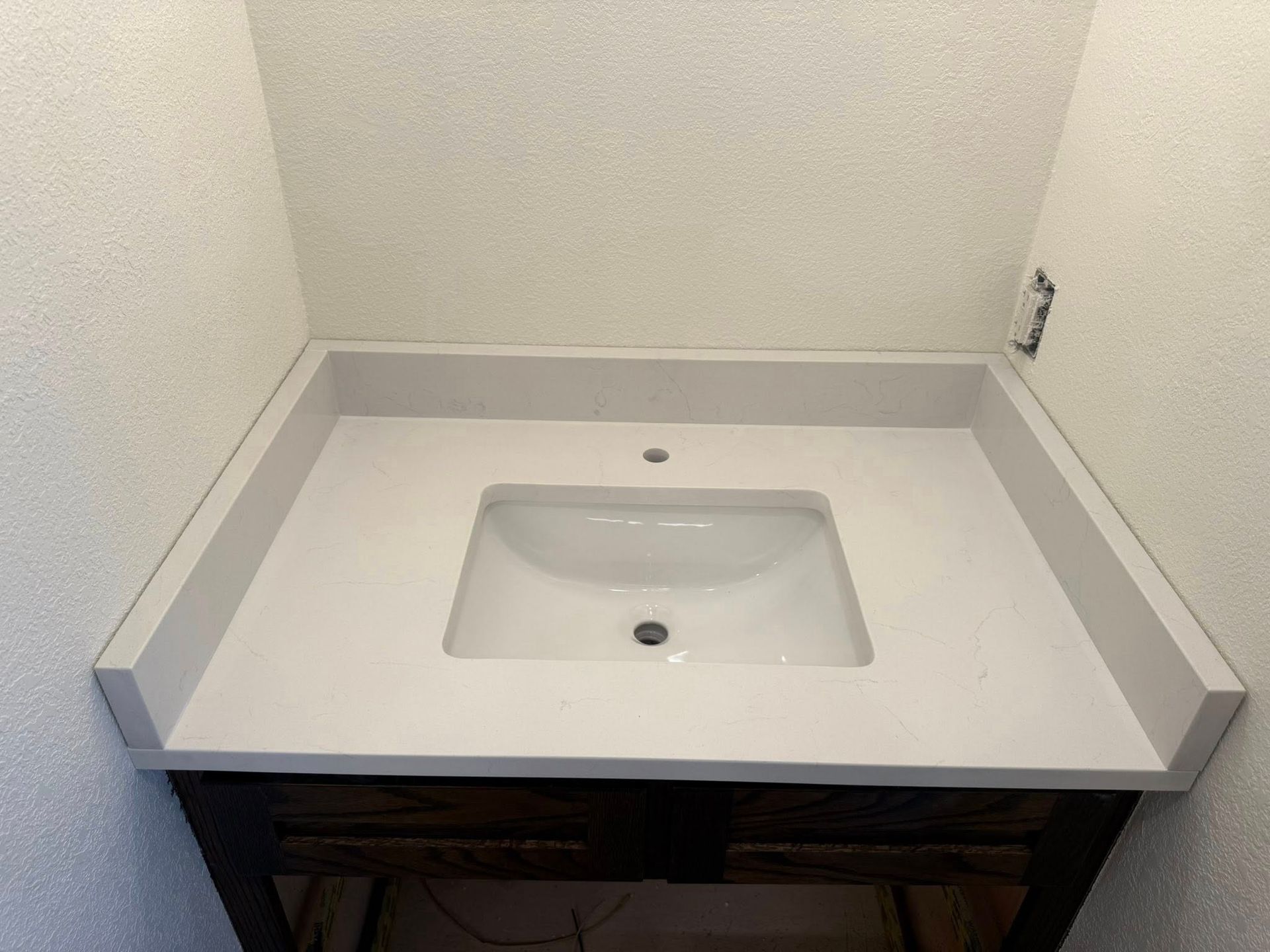 White bathroom vanity with a rectangular sink and countertop in a small alcove