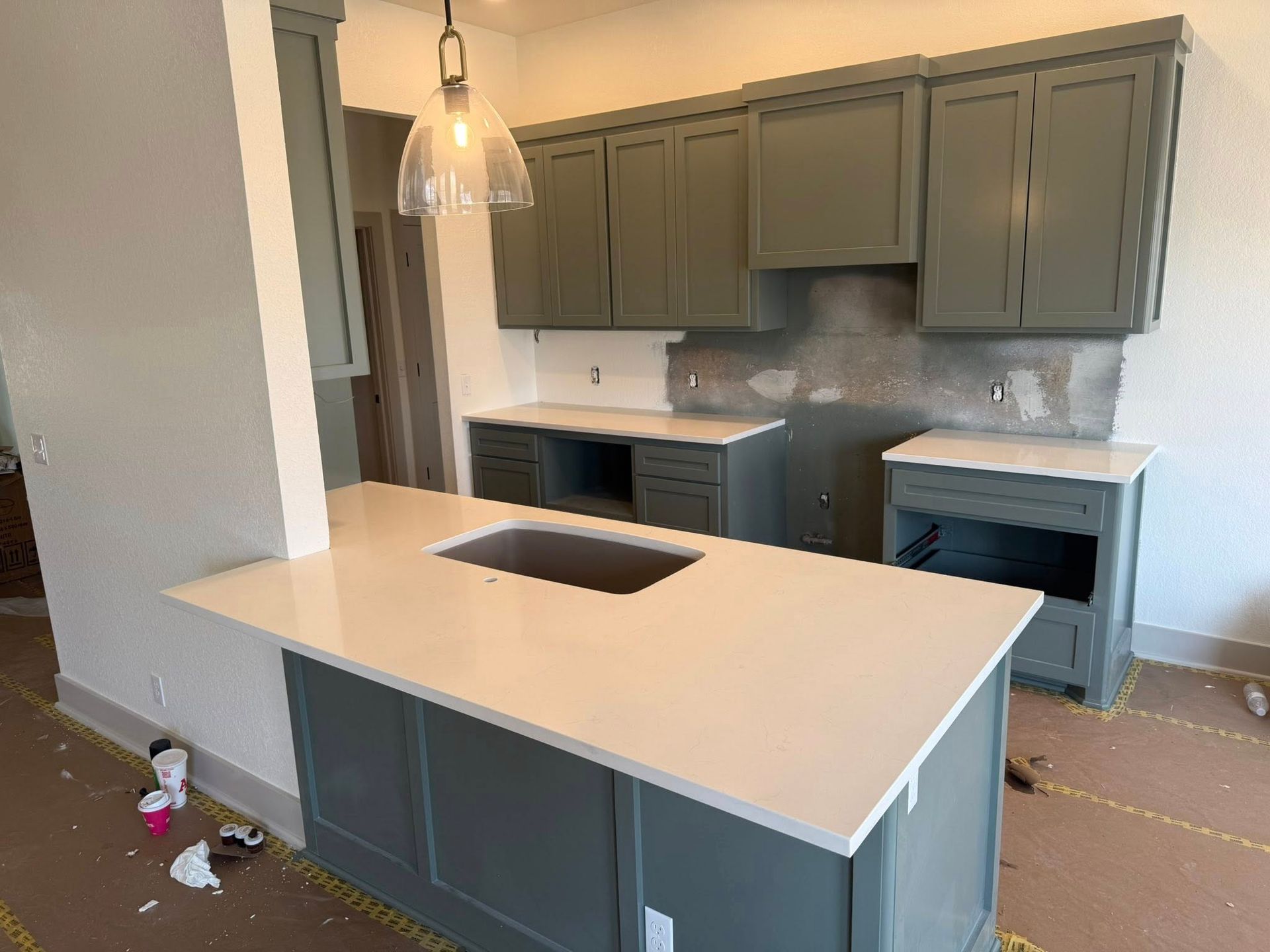 Empty modern kitchen with gray cabinets, white island, and pendant lights under construction