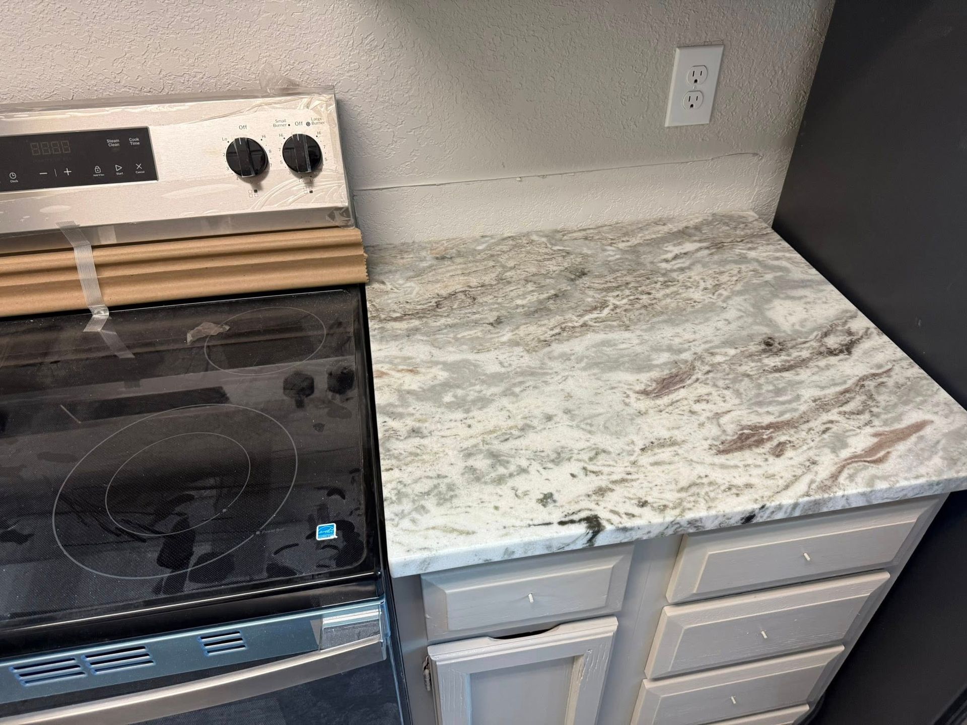 Kitchen stove beside gray cabinets with a light marble-look countertop and white wall outlet.