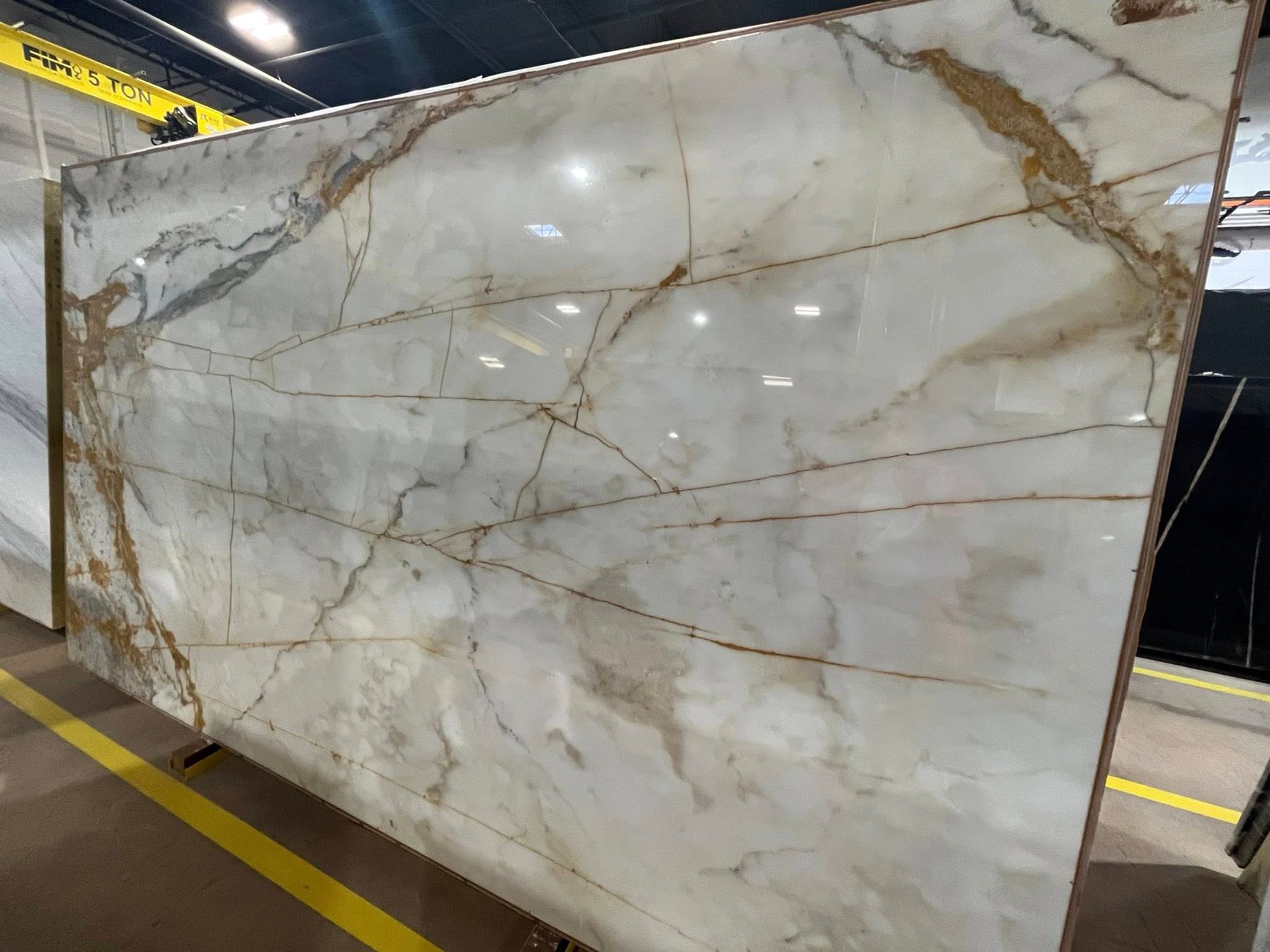 Large polished white marble slab with gray and gold veining in an industrial warehouse