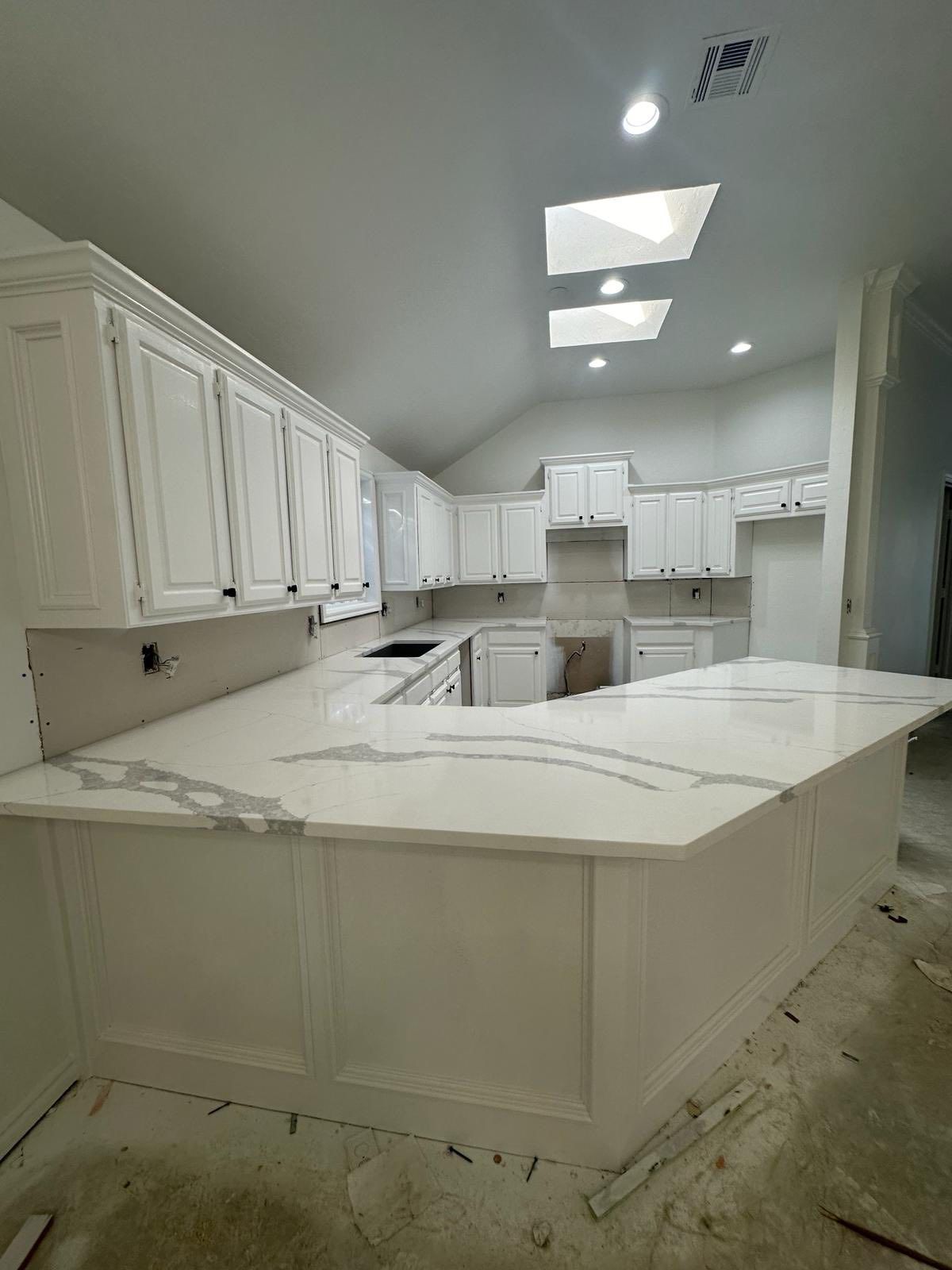 Bright white kitchen with marble island, cabinets, and skylights in a modern interior