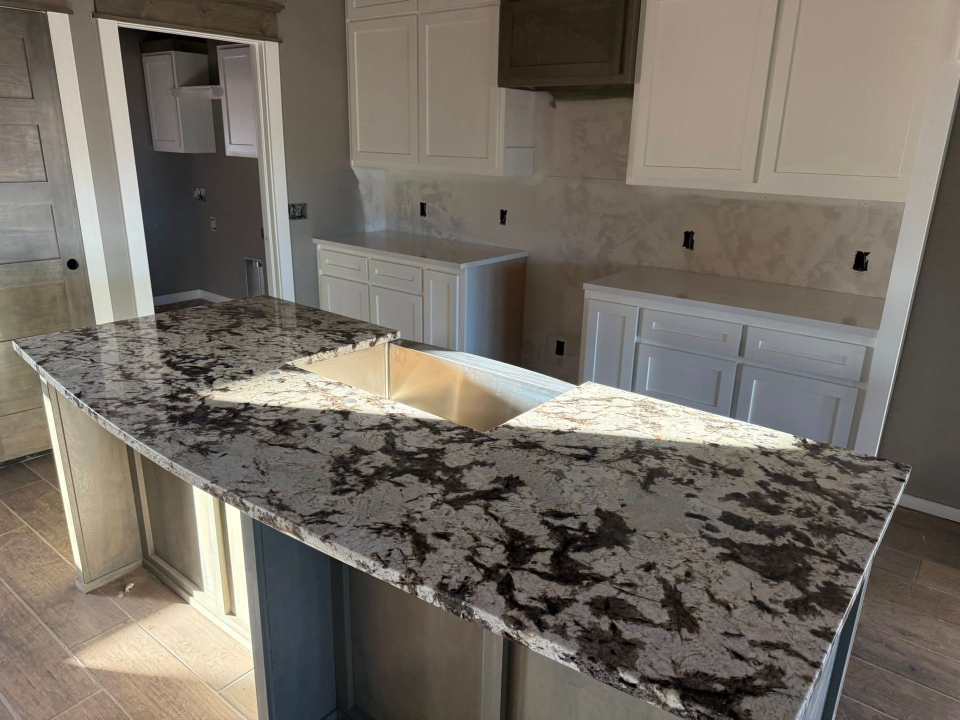 Kitchen with large dark granite island and white cabinets under warm natural light