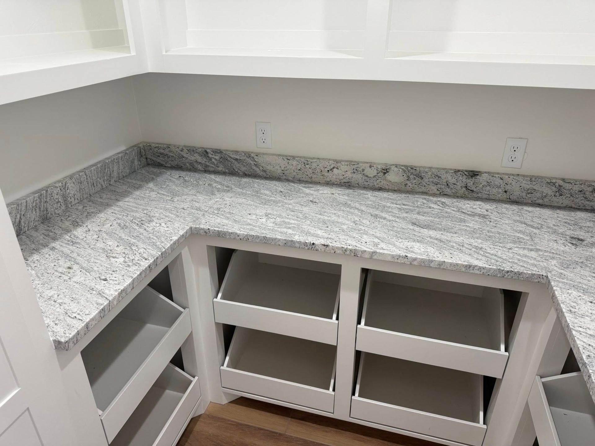 Unfinished L-shaped kitchen countertop with gray granite and open cabinet shelves below