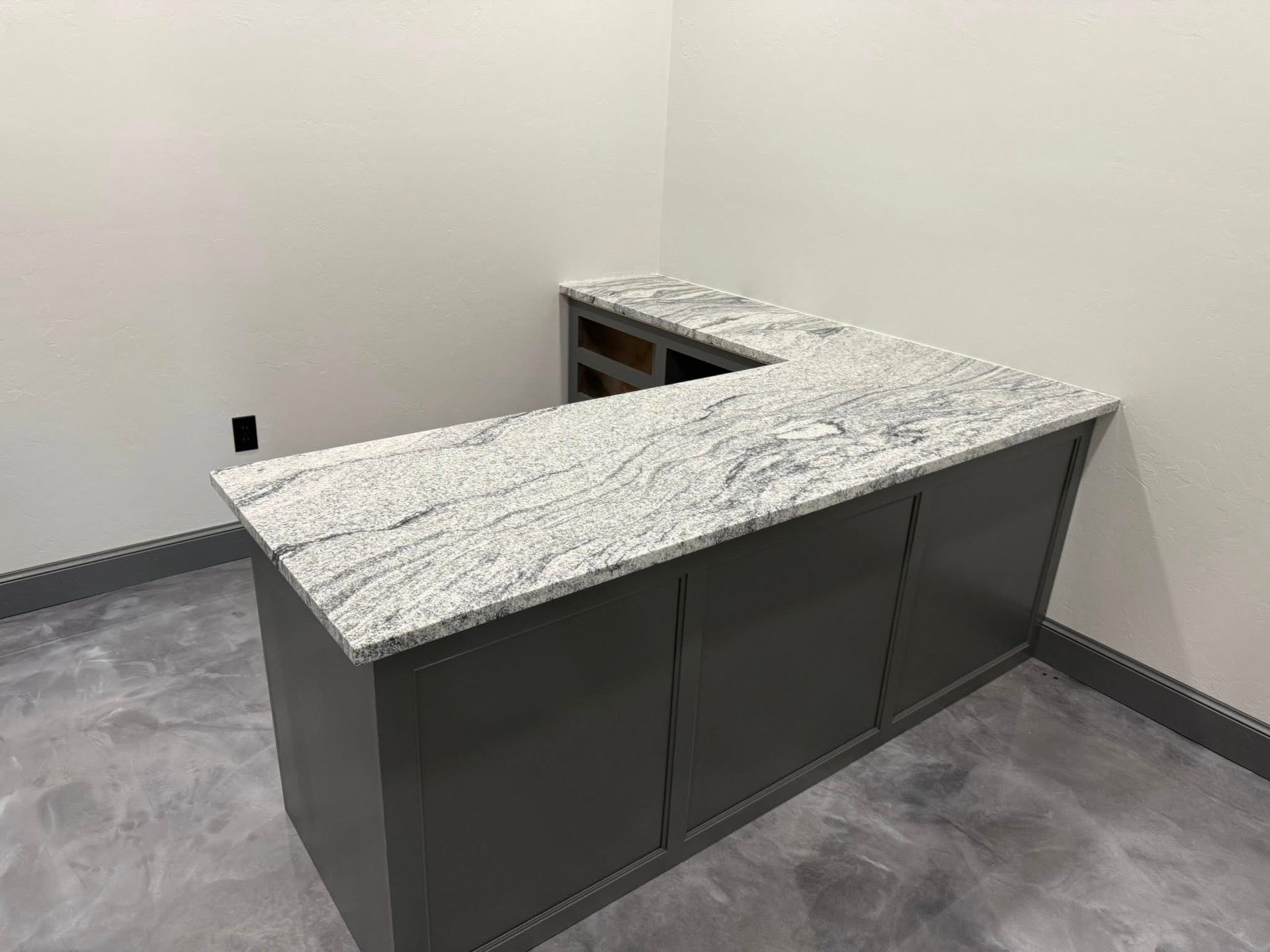 Modern kitchen island with dark cabinets and a light speckled countertop in a small room