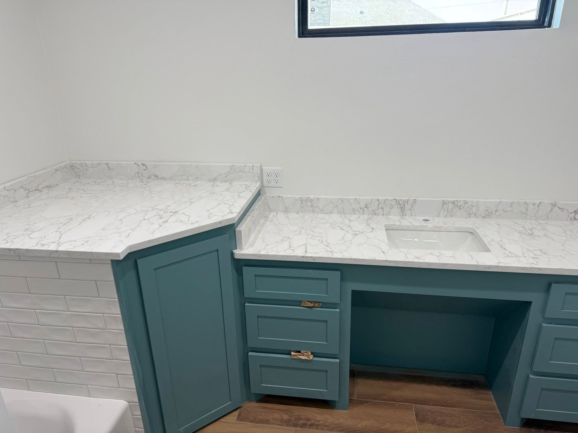 Teal kitchen cabinets with white marble countertops and a small window above