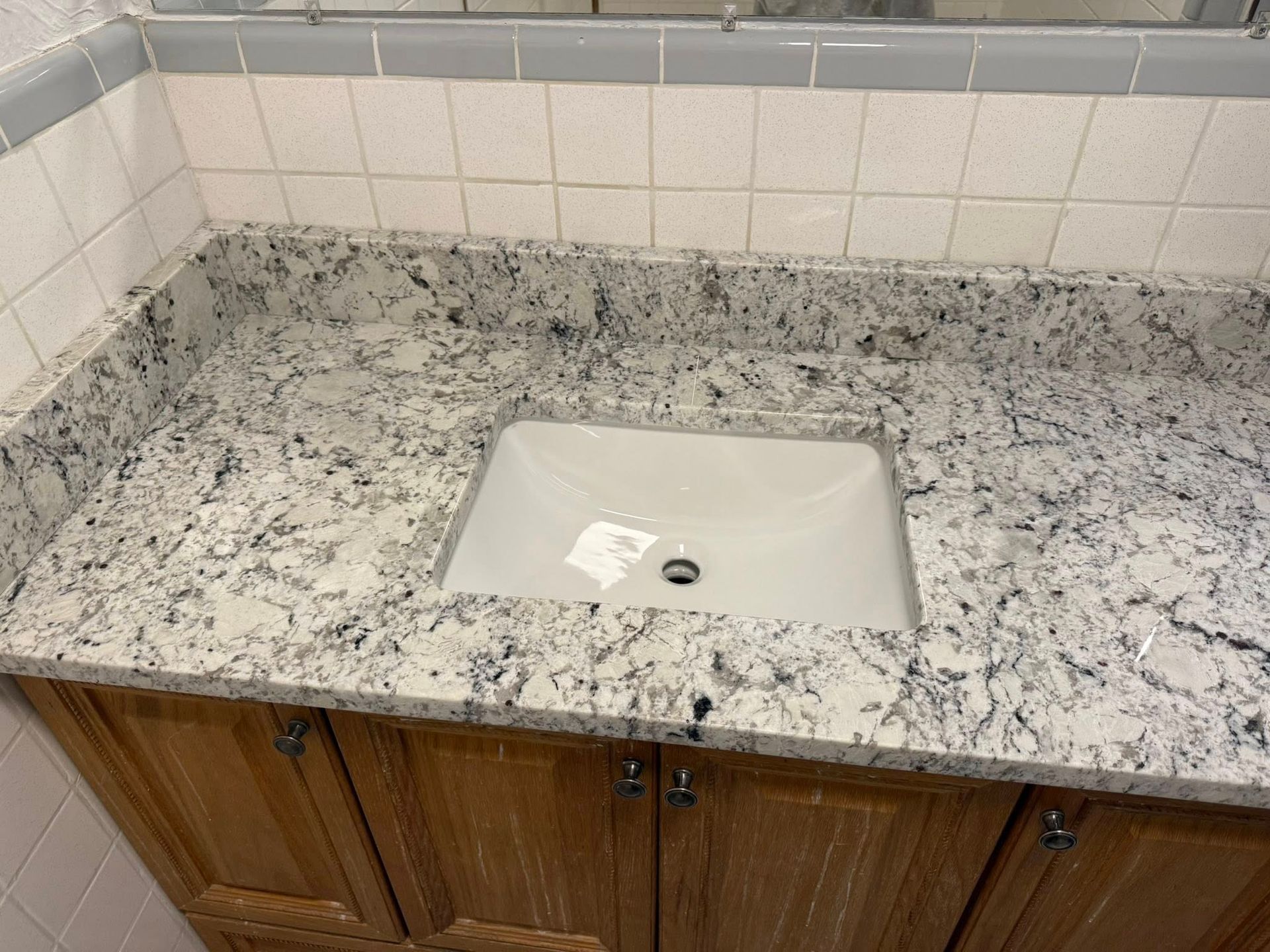 Bathroom vanity with granite countertop and white sink beneath tiled backsplash