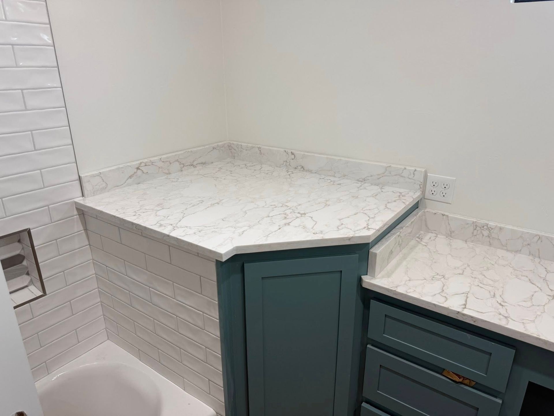 Corner kitchen countertop with white marble-look surface and teal cabinets below