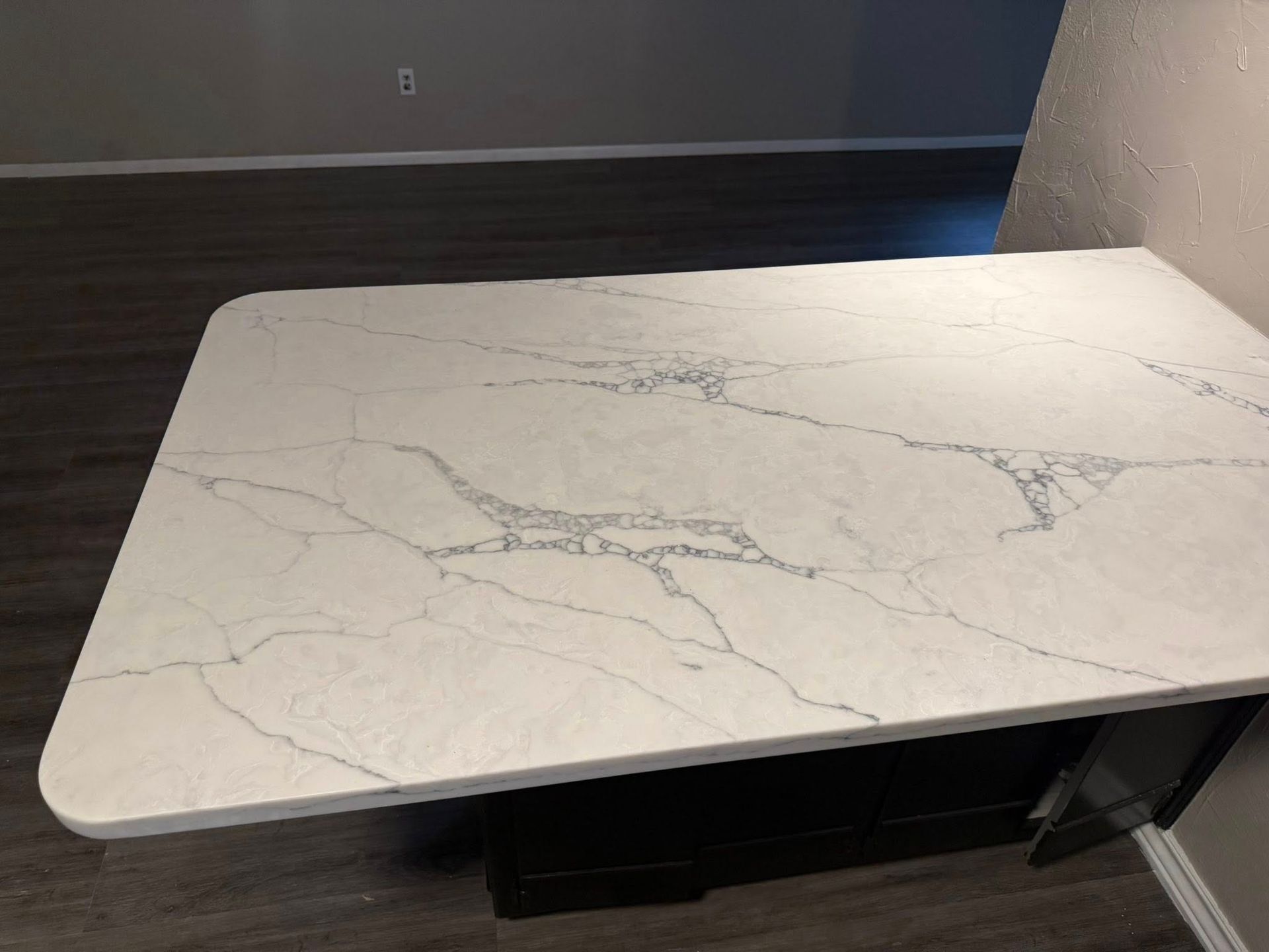 White marble-look tabletop beside a gray wall and dark floor, with black storage below