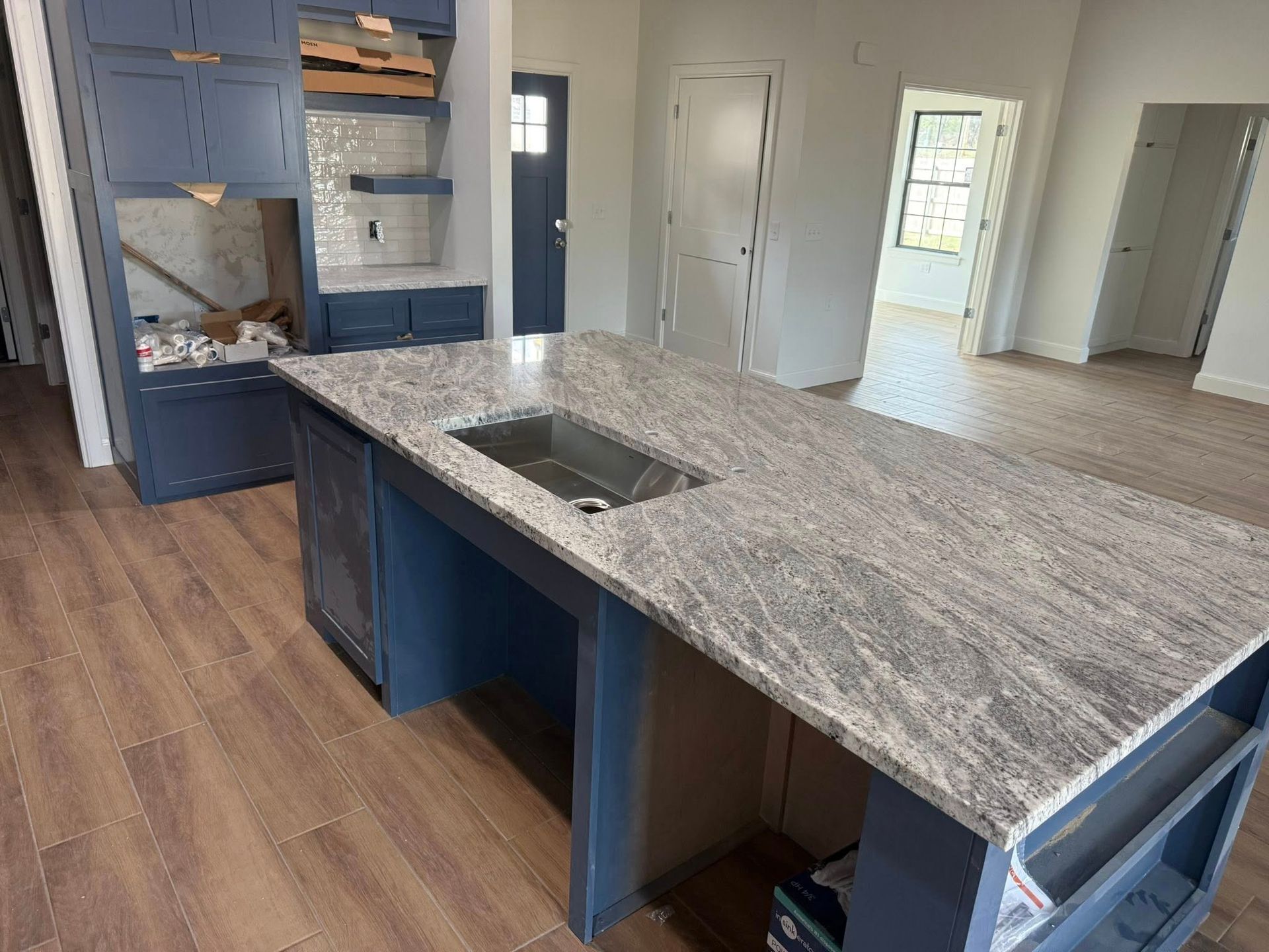 Modern kitchen with gray island countertop, blue cabinets, and wood-look flooring in a bright open room