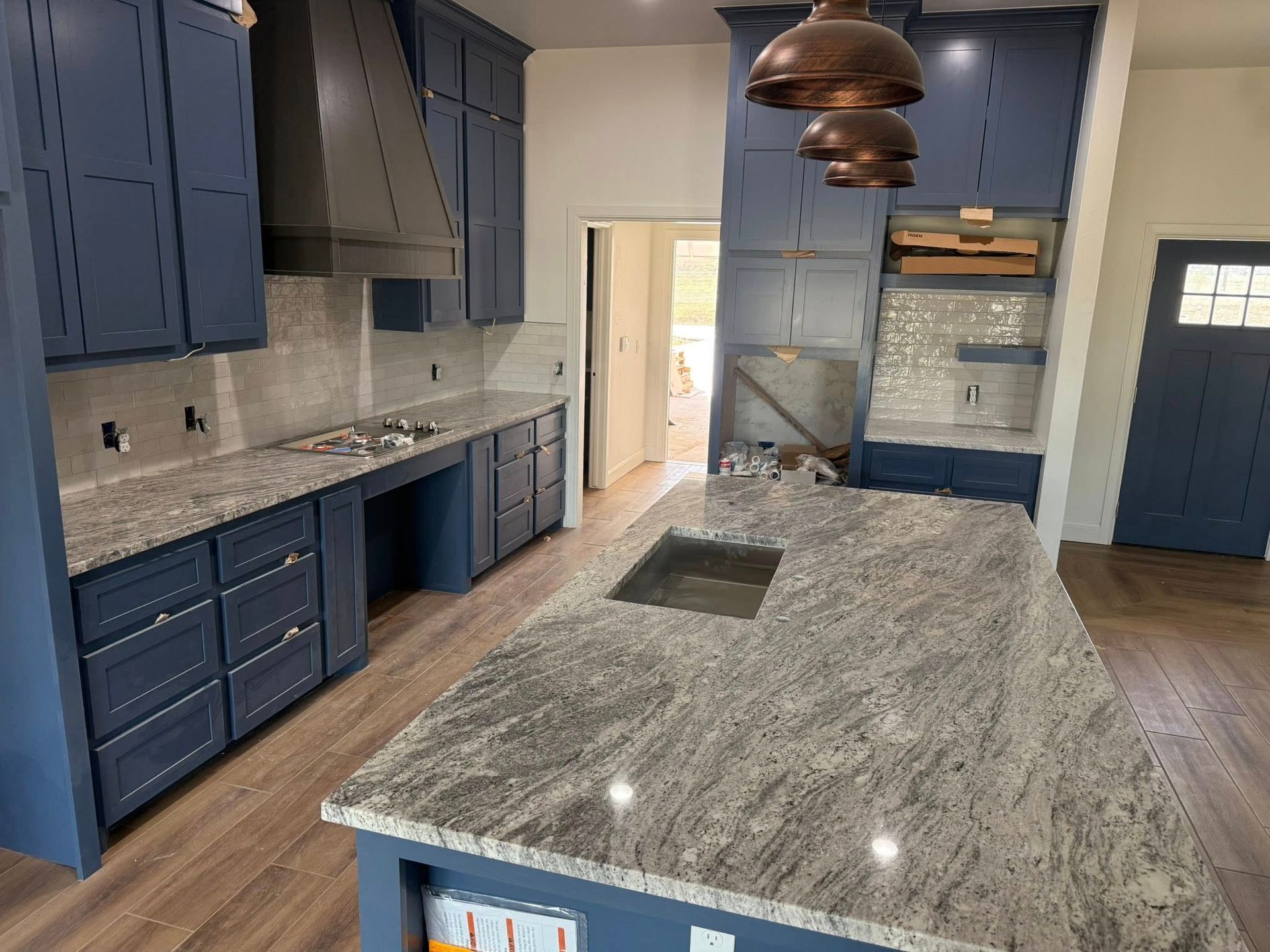 Modern kitchen with blue cabinets, gray stone island, pendant lights, and wood flooring.