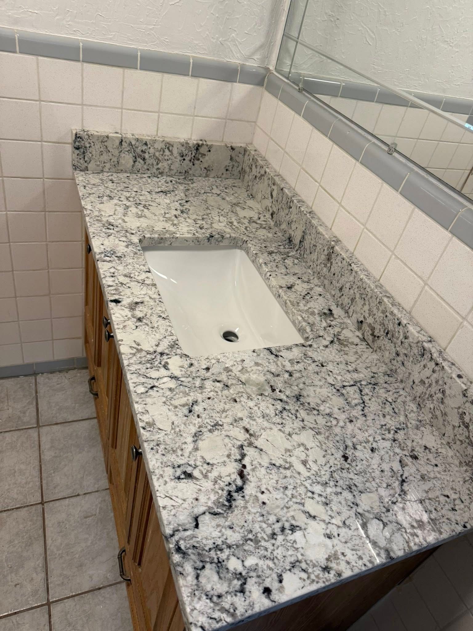 Granite bathroom countertop with white sink and tiled walls