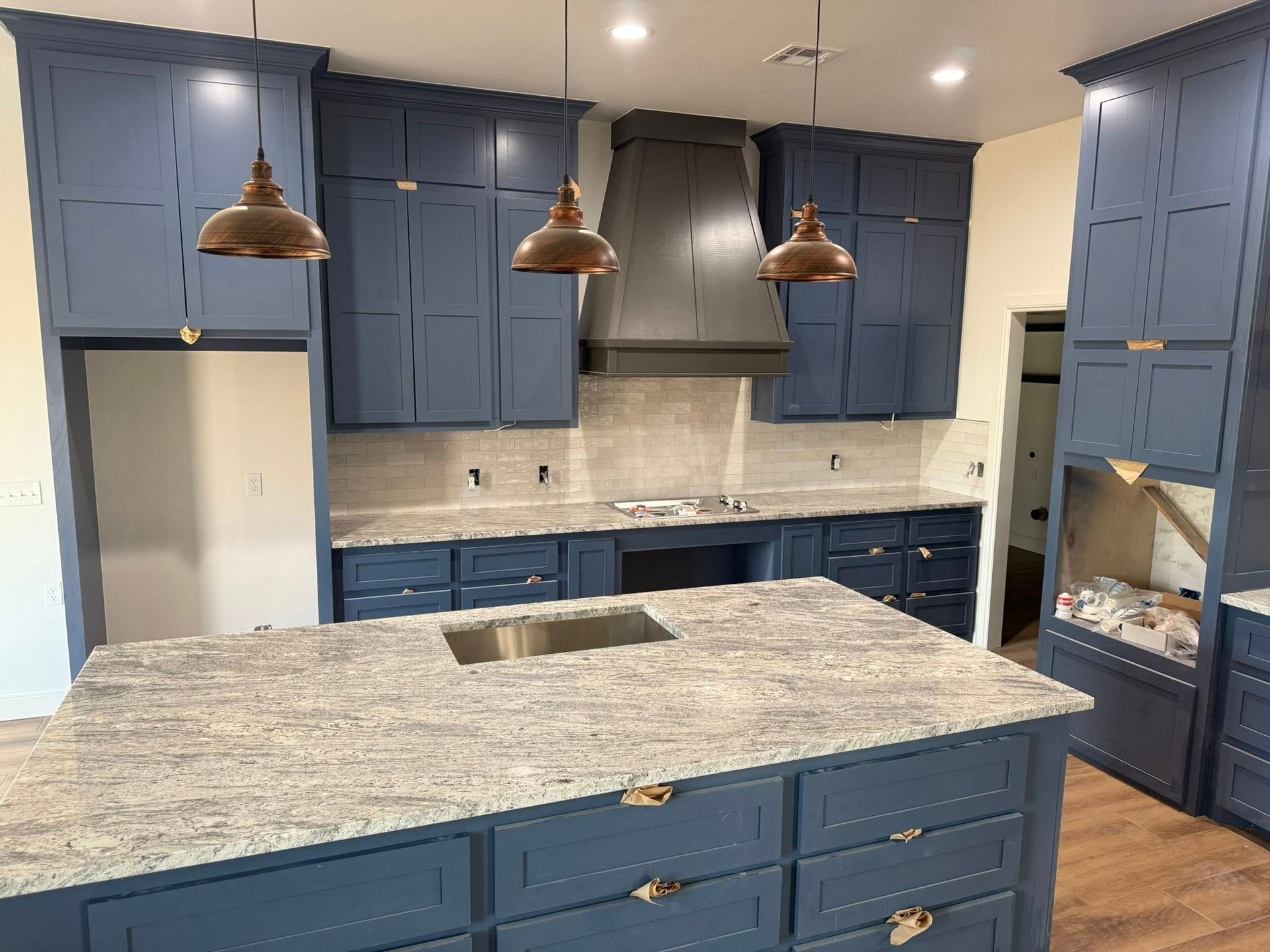 Blue kitchen with granite island, copper pendant lights, and stainless range hood