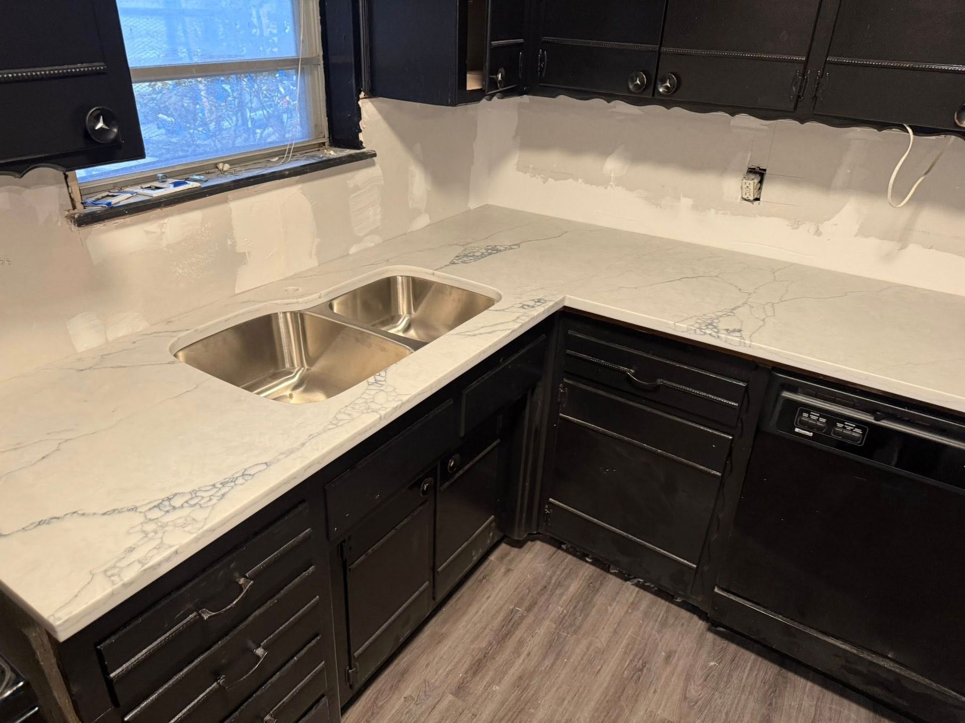 Modern kitchen corner with black cabinets, white countertops, and a stainless steel sink by the window