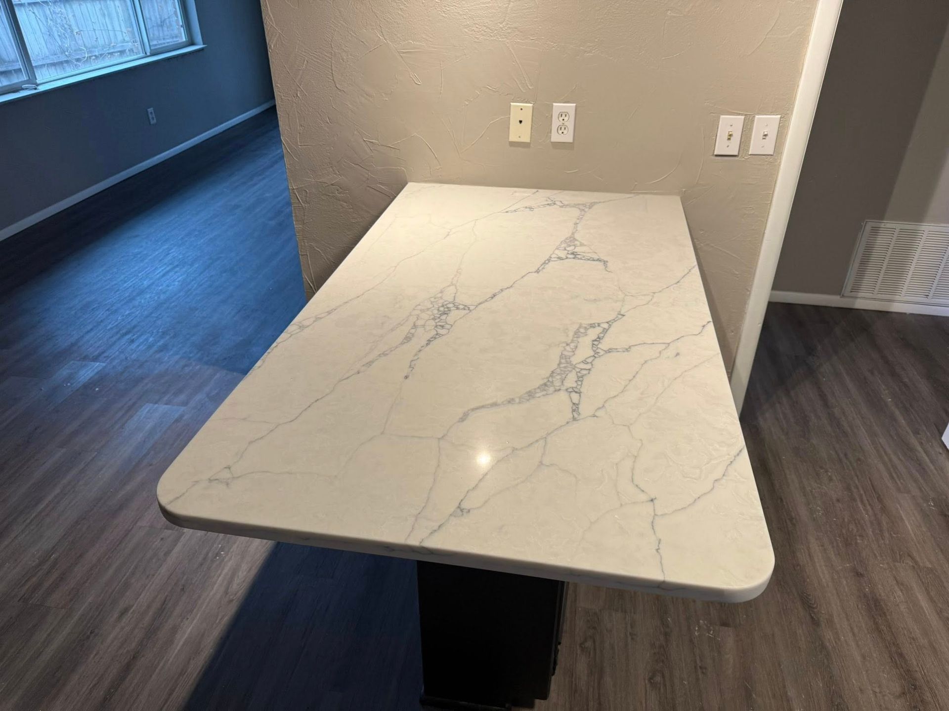 Marble-look table with black base in a room with wood flooring and wall outlets