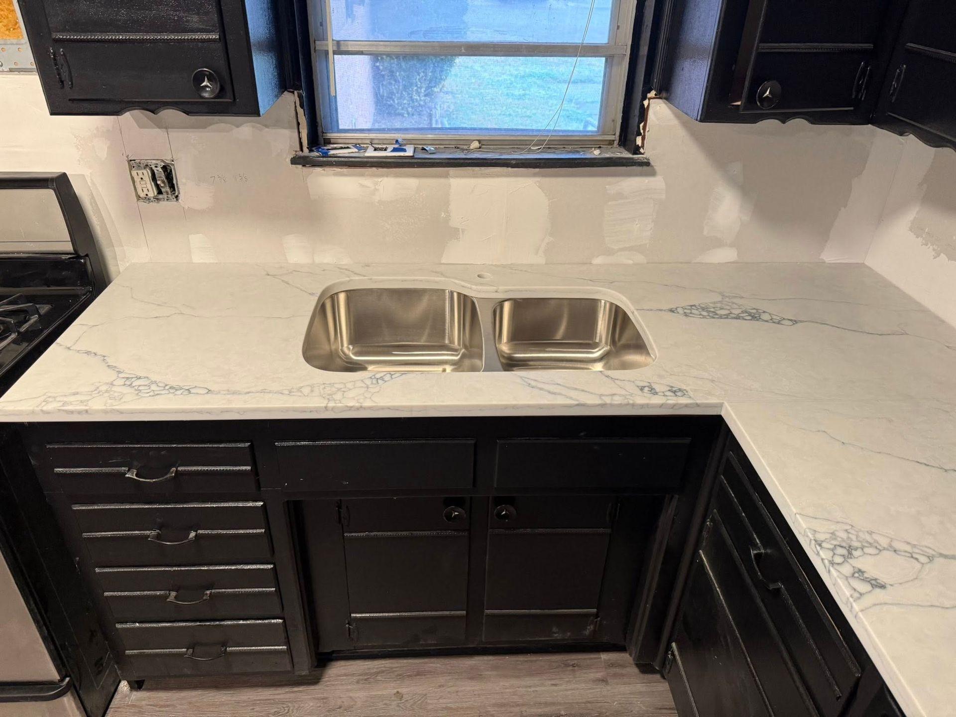 Modern kitchen with white countertop, double sink, black cabinets, and window above the sink
