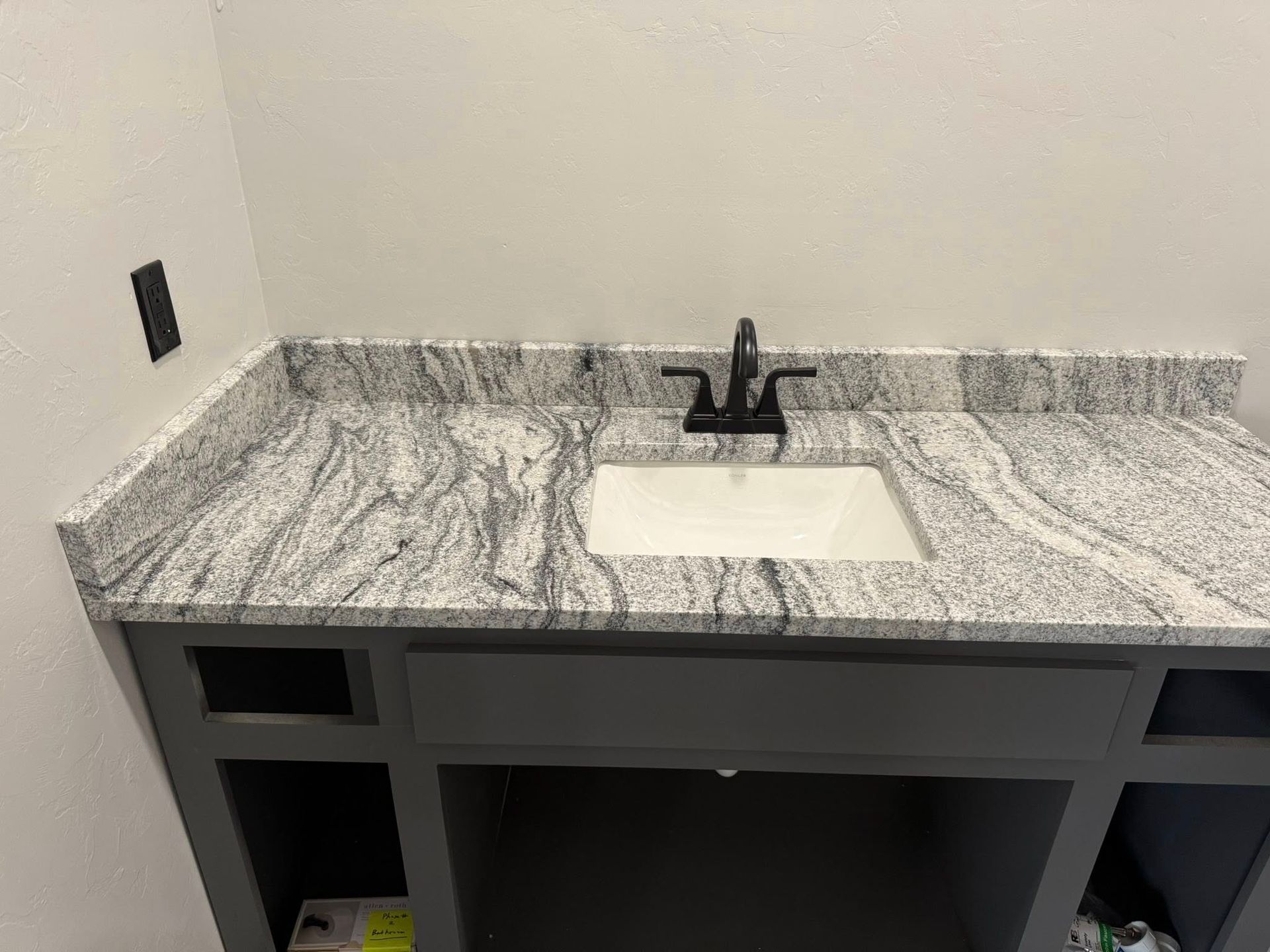 Gray marble bathroom vanity with black faucet and white sink against a light wall