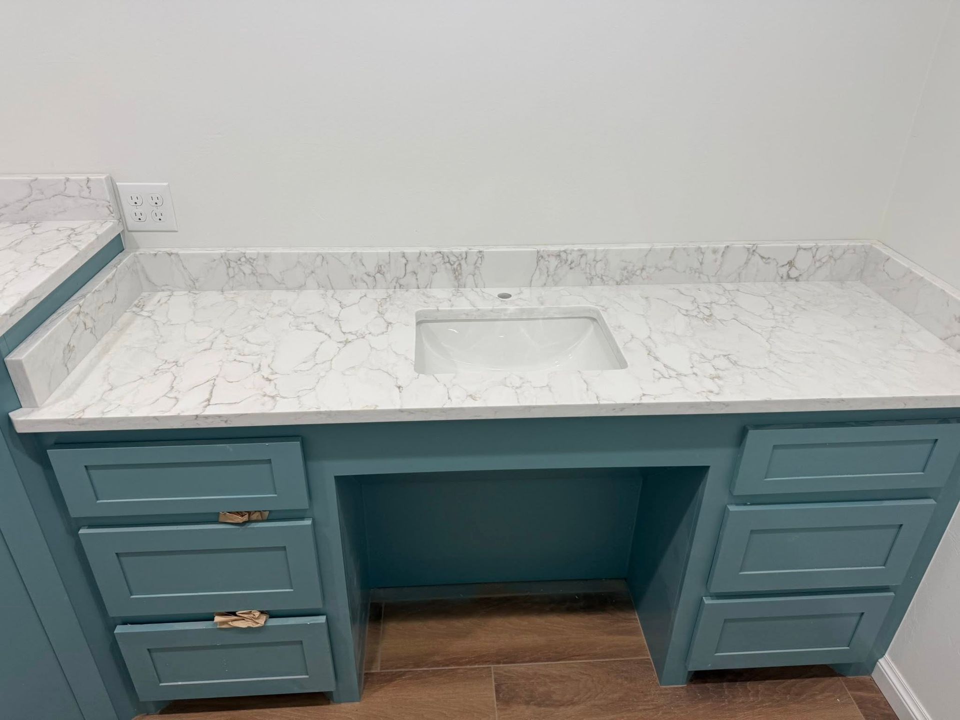 Teal bathroom vanity with marble-look countertop and built-in sink, showing open center cabinet space