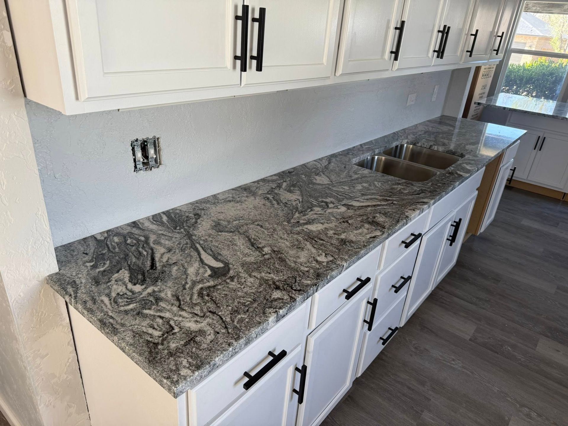 Kitchen with white cabinets, gray patterned granite countertop, and stainless-steel sink by a window