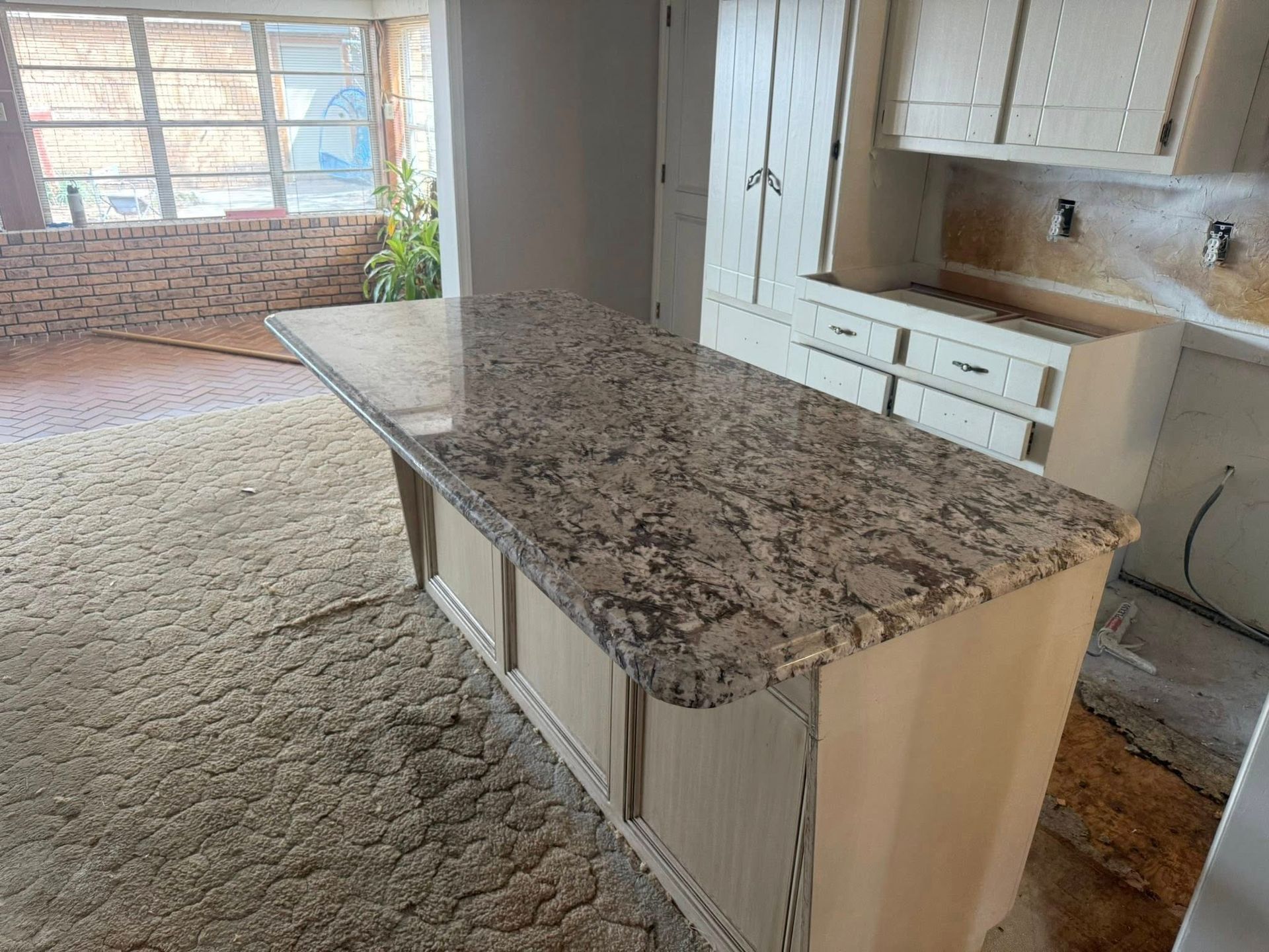 Kitchen island with granite countertop in an unfinished open-concept room with carpet and large windows