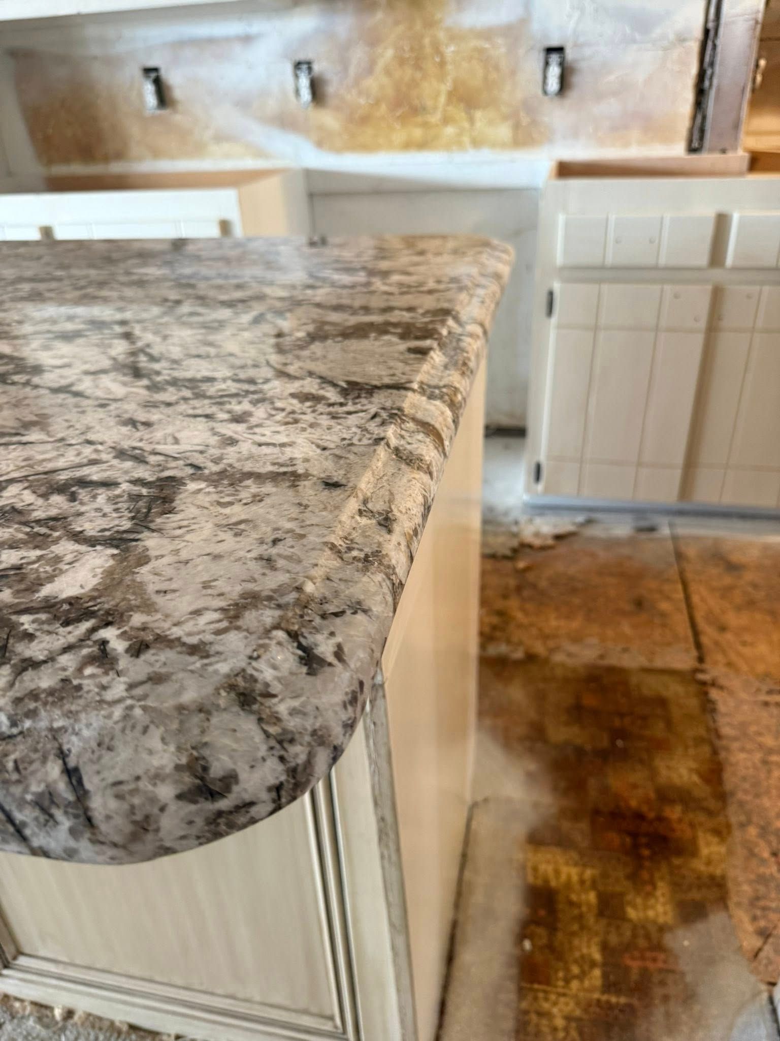 Granite kitchen countertop with rounded edge beside a tiled floor and cabinets