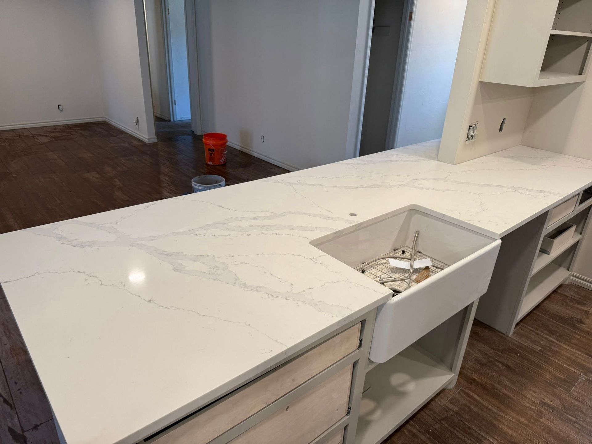 Kitchen with white marble island and built-in sink, unfinished cabinets, and hardwood floor in the background
