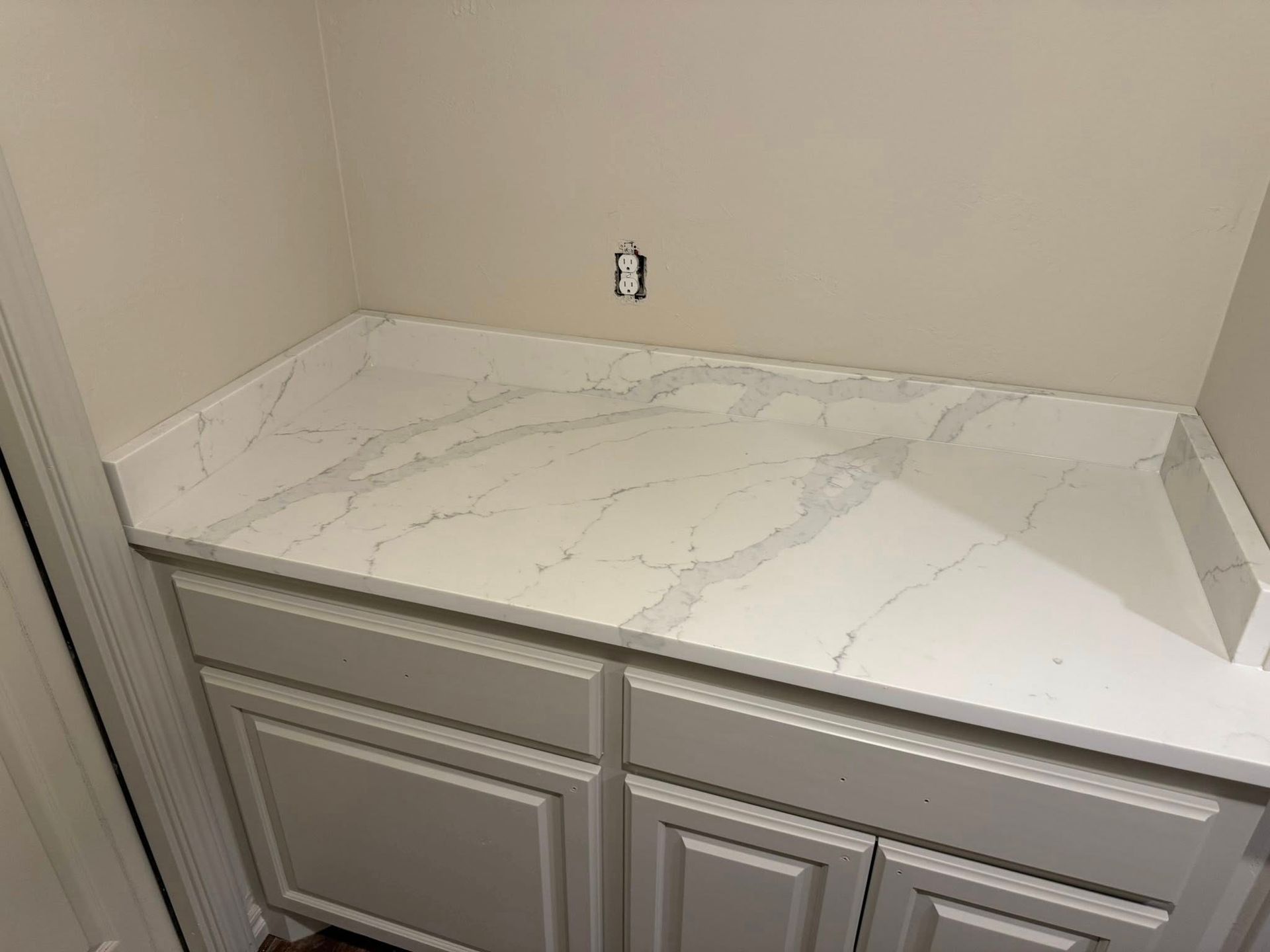White marble-look countertop with gray veining above cream cabinet doors in a corner alcove.
